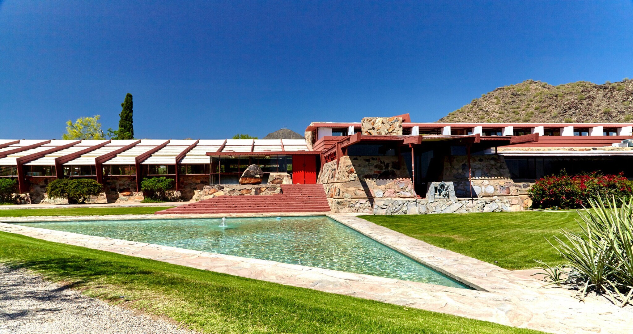 Flaches Gebäude, im Vordergrund ein dreieckiger Pool