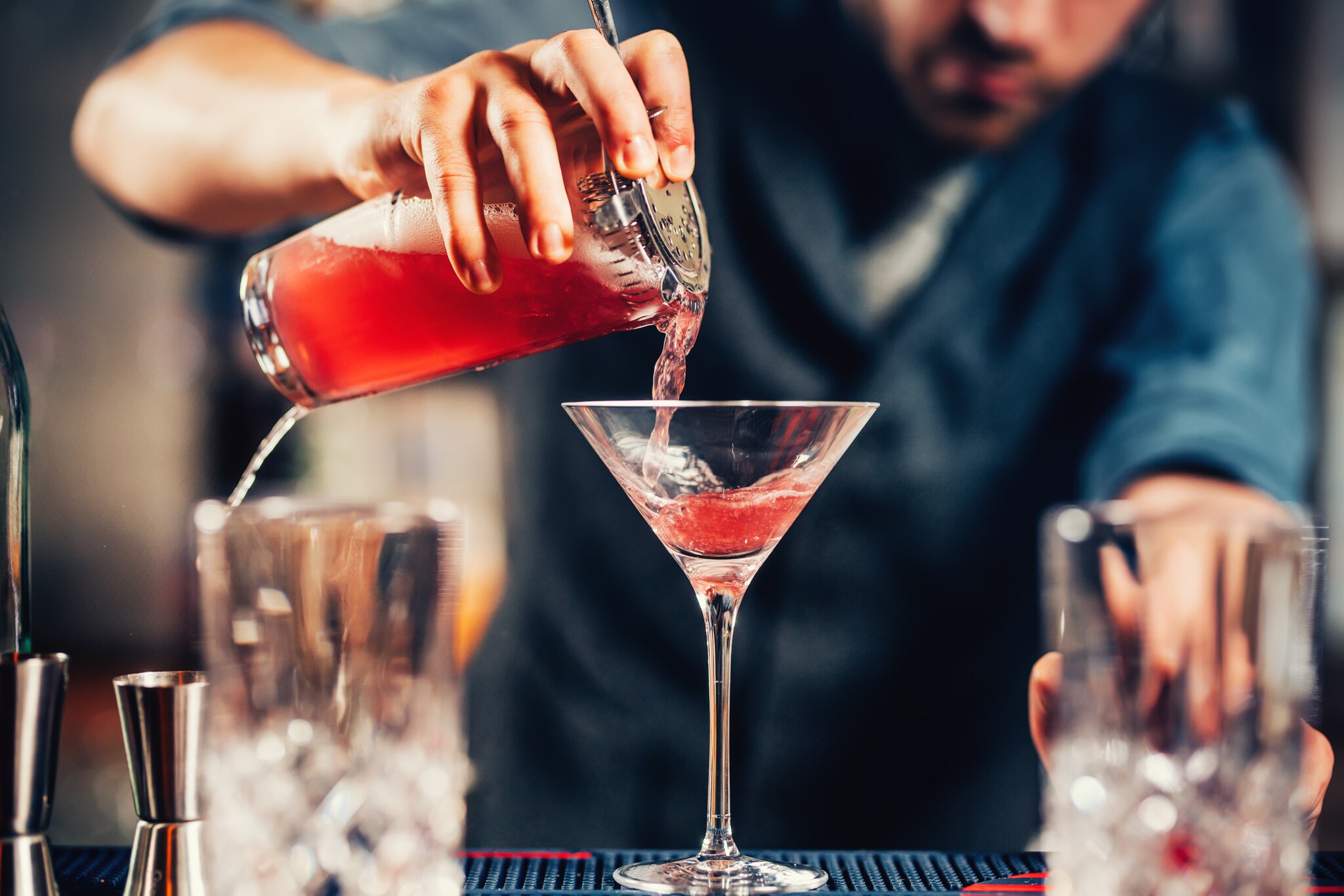 Nahaufnahme eines Cocktailglases, das von einem Barkeeper mit einer roten Flüssigkeit gefüllt wird