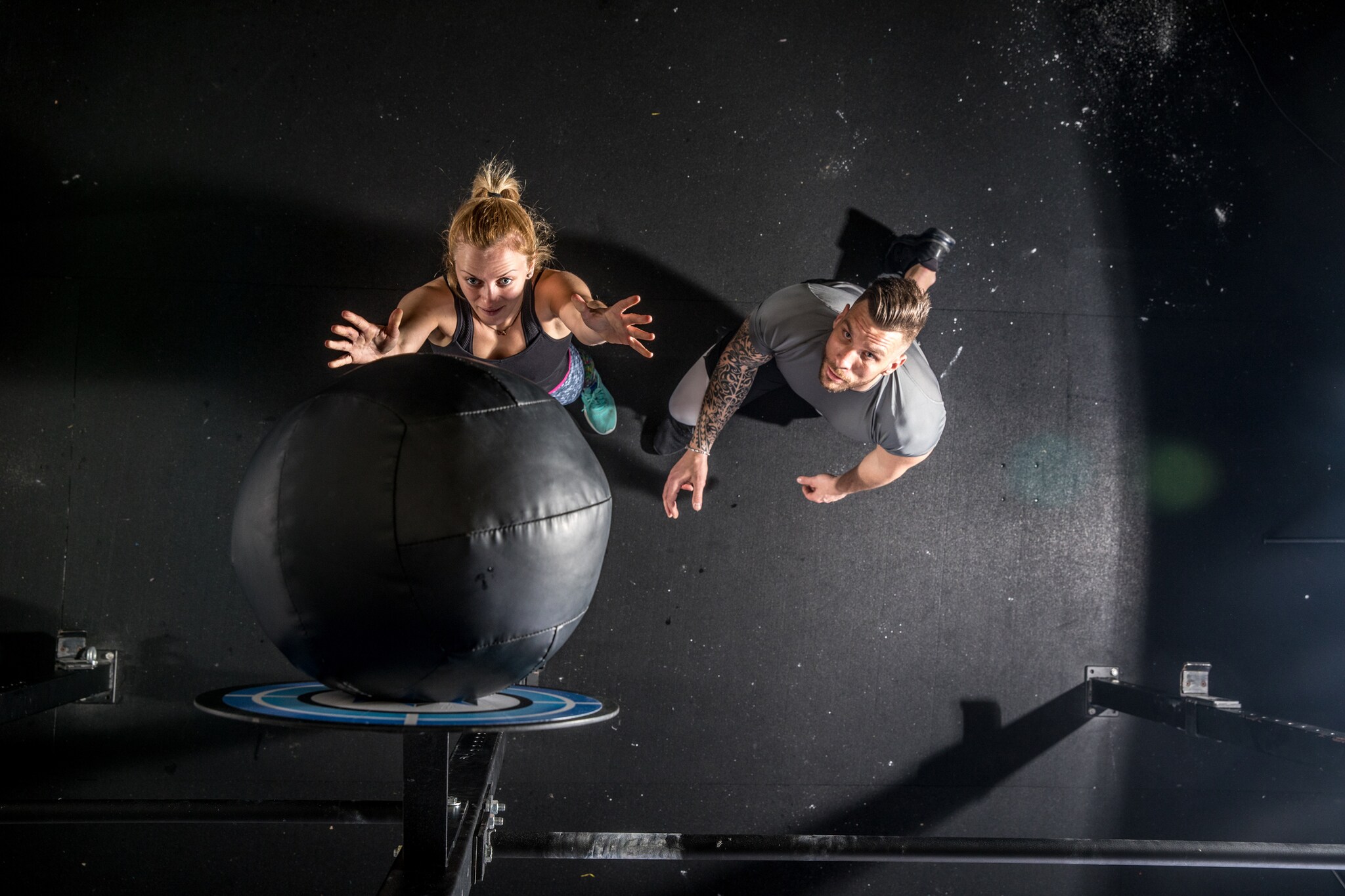 Eine Frau, die einen Medizinball wirft, und ein neben ihr stehender und ebenfalls nach oben blickender Mann