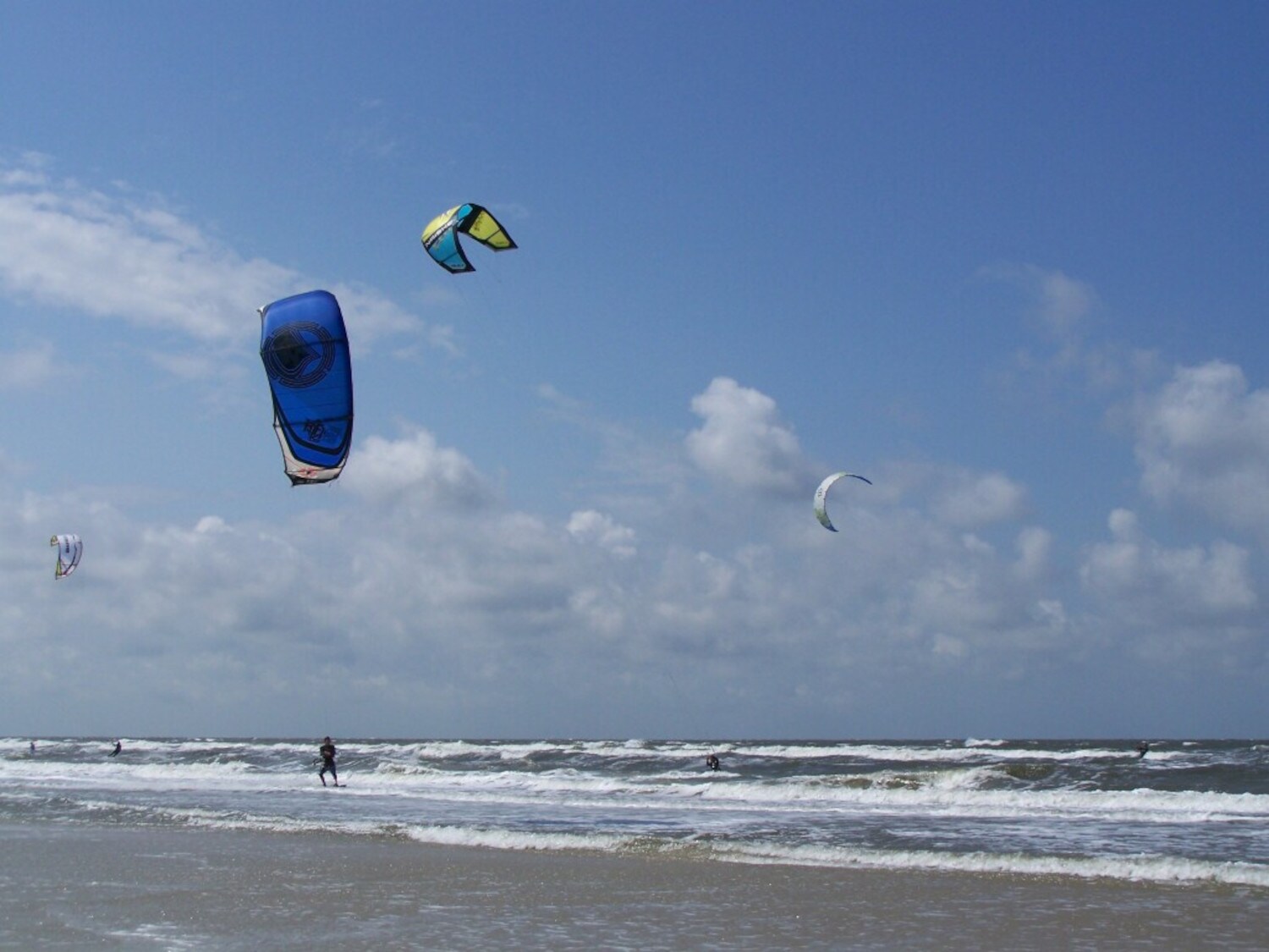 Kiteboarder gleiten am Strand von Juist durch die Wellen.