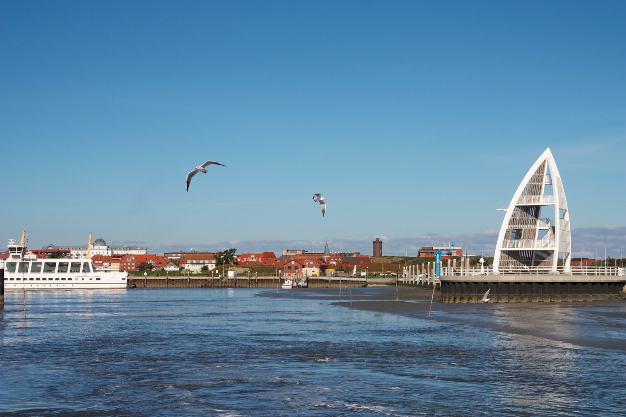 Blick auf die Fähre und den Sportboothafen von Juist mit dem Seeschild. Möwen fliegen im Vordergrund.