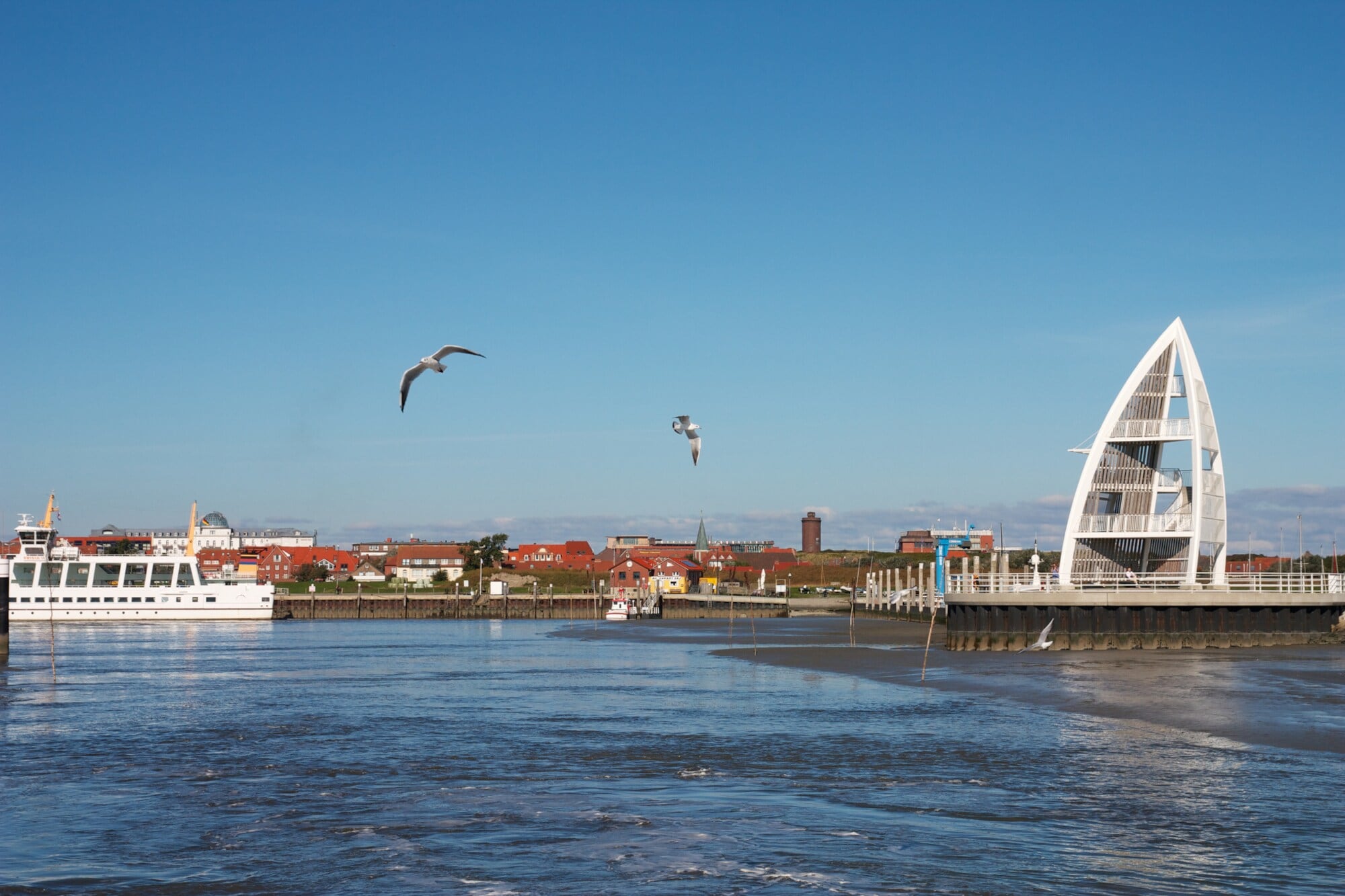 Blick auf die Fähre und den Sportboothafen von Juist mit dem Seeschild. Möwen fliegen im Vordergrund. Blick auf die Fähre und den Sportboothafen von Juist mit dem Seeschild. Möwen fliegen im Vordergrund.
