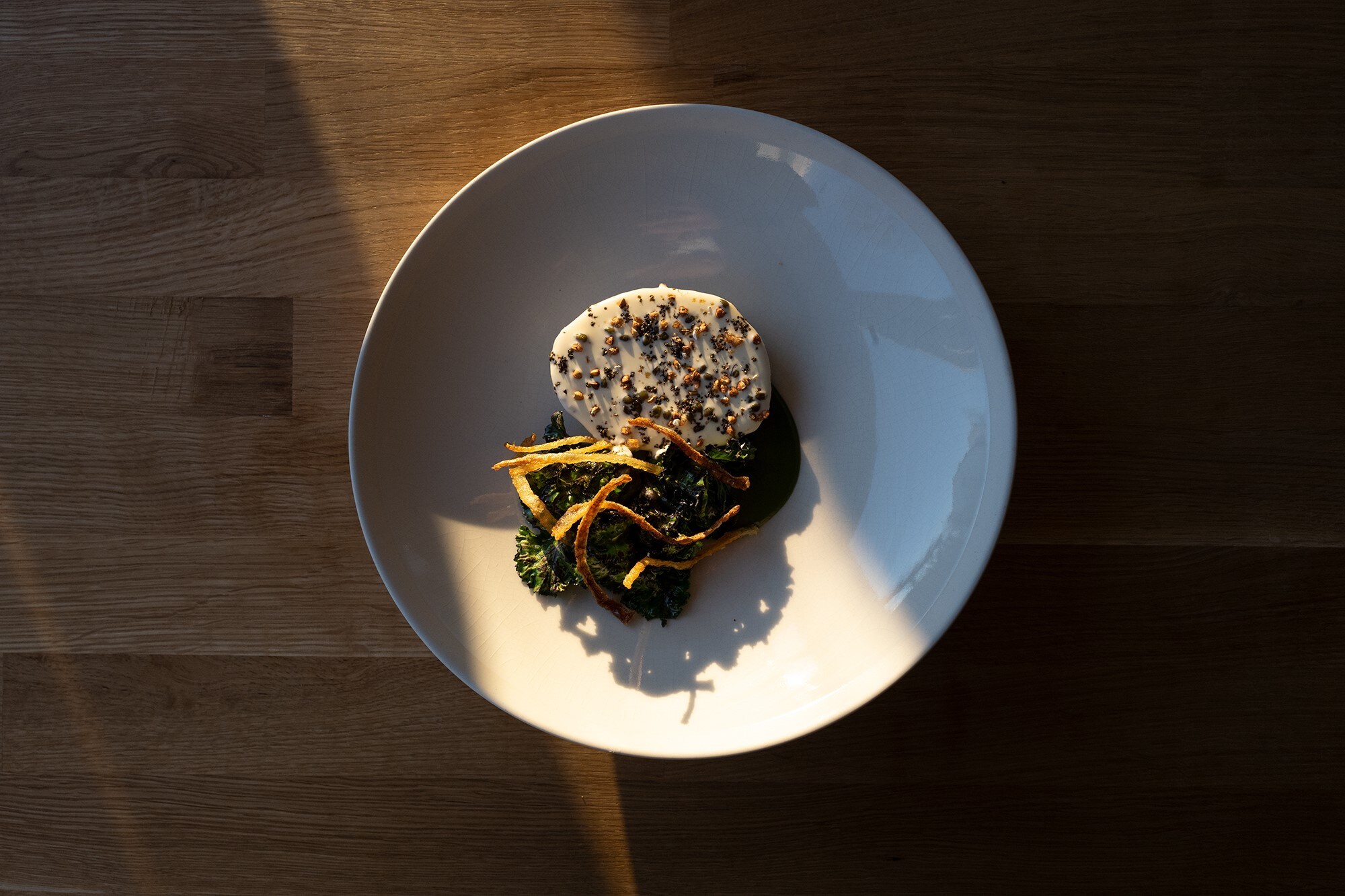 Weißer Teller mit weißen und grünen Speisen auf einem Holztisch