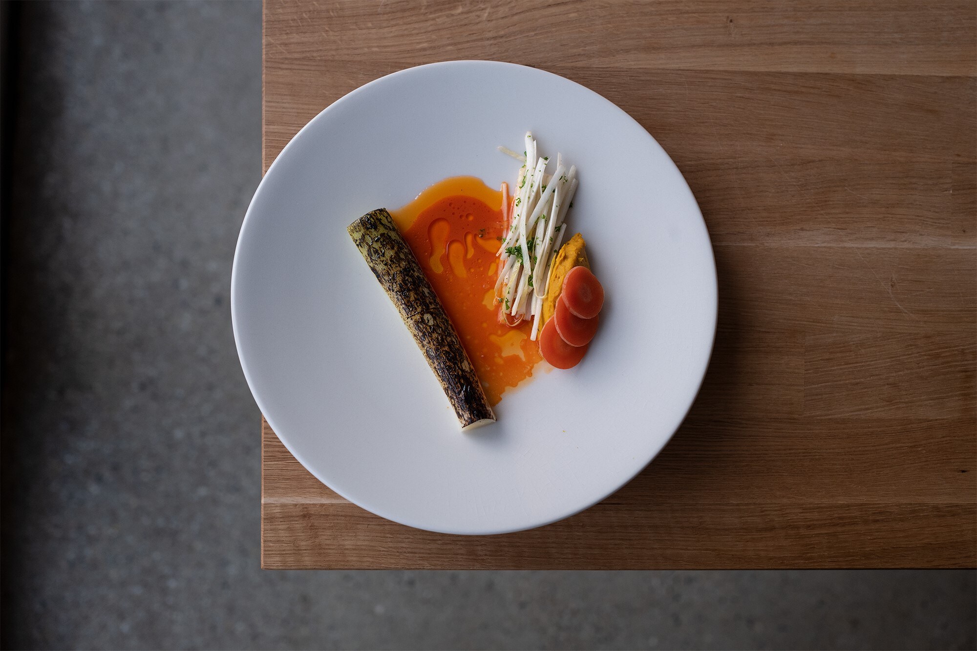 Weißer Teller mit Karotten in Soße auf einem braunen Holztisch