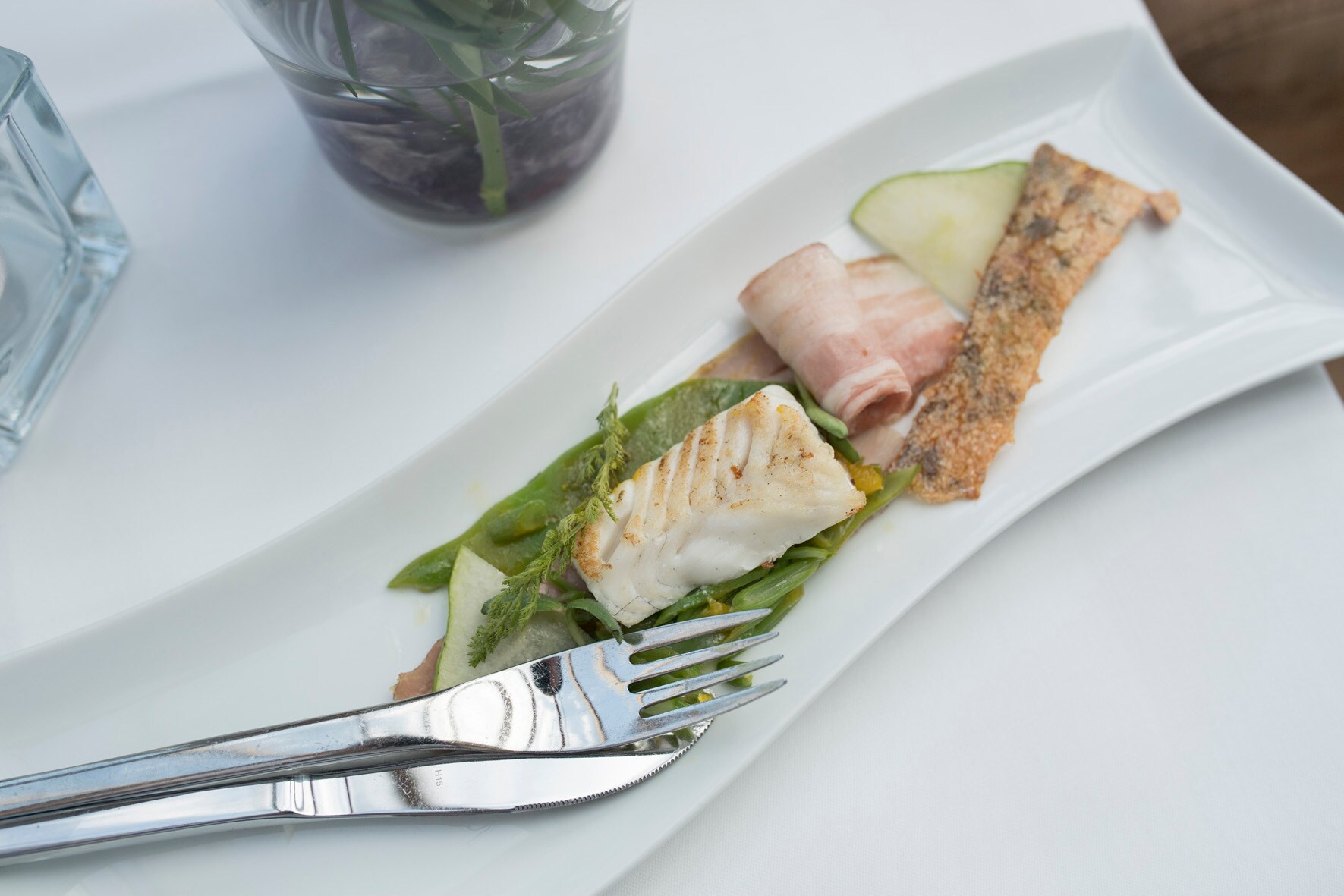 Fisch und Fleisch auf einem länglichen, geschwungenen, weißen Porzellanteller