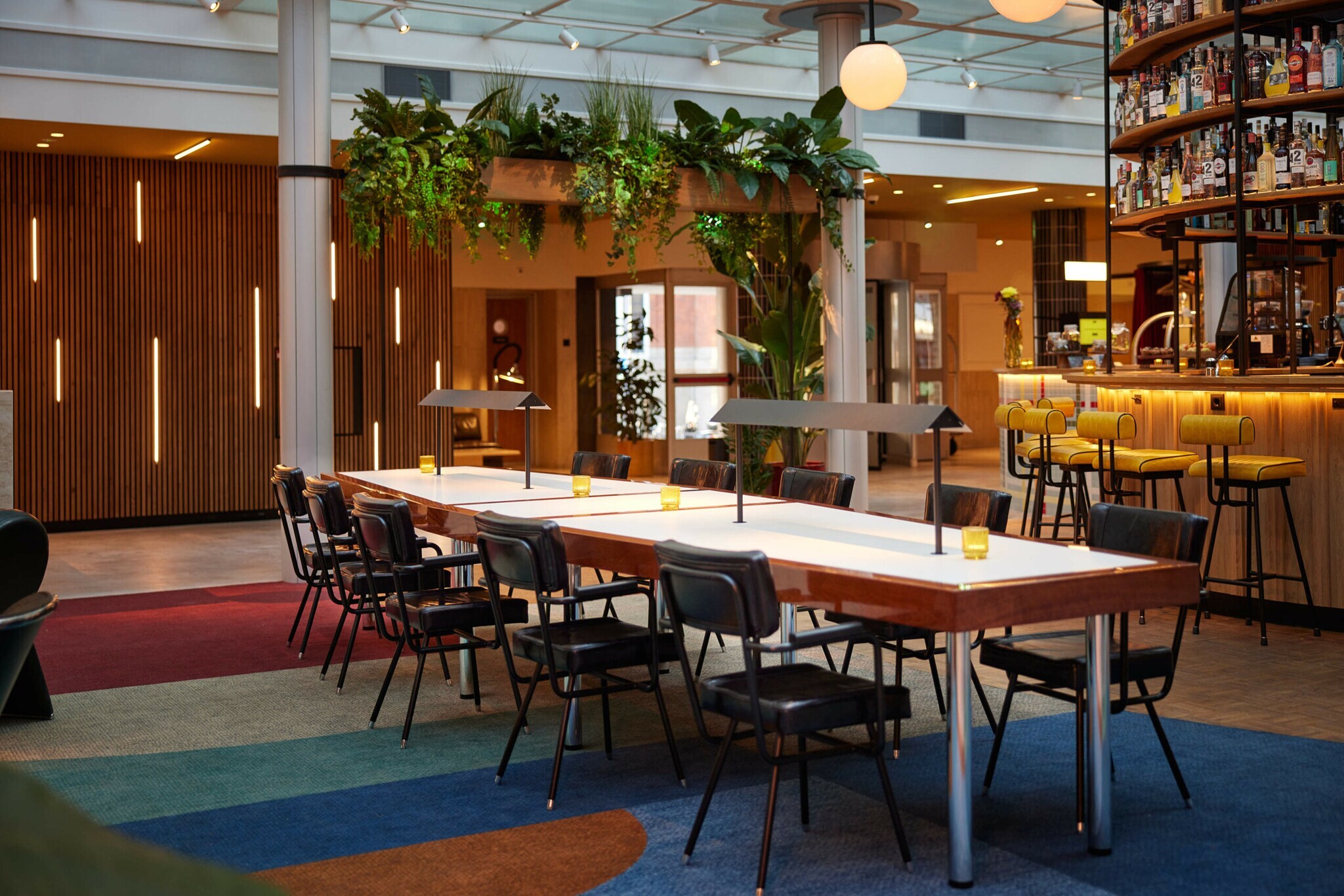 Langer Tisch mit Stühlen in einer Hotel-Lobby, im Hintergrund eine beleuchtete Bar