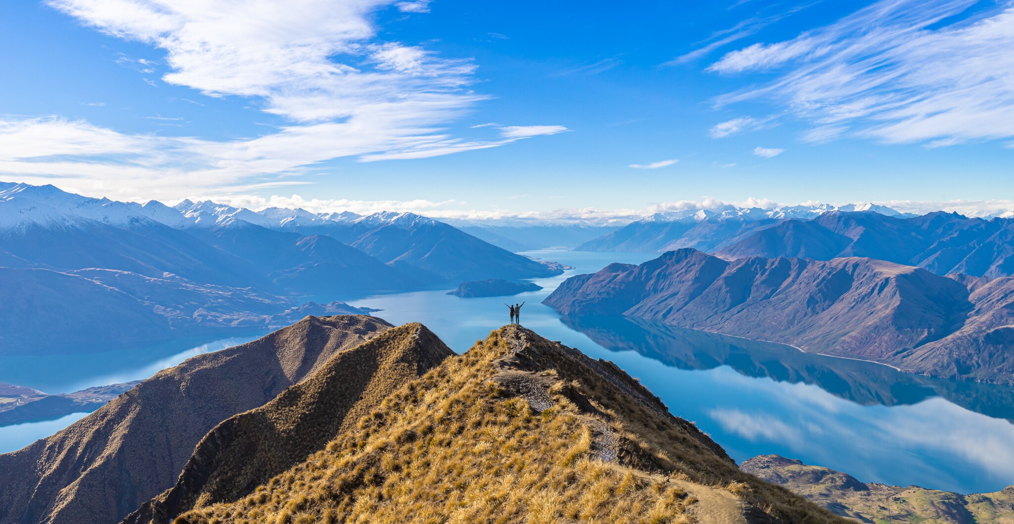 Ein Paar steht auf einem Gipfel vor Seenlandschaft und Bergpanorama der Neuseeländischen Alpen