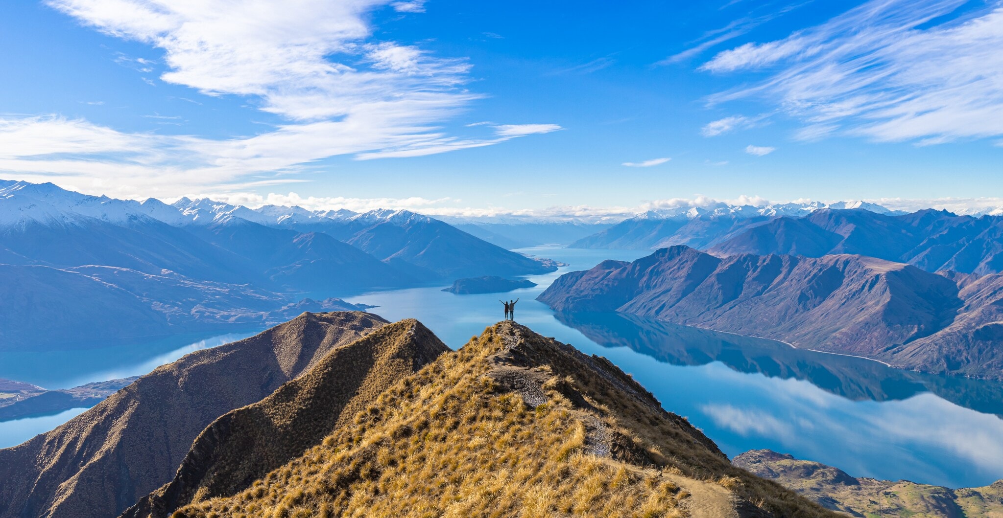 Ein Paar steht auf einem Gipfel vor Seenlandschaft und Bergpanorama der Neuseeländischen Alpen Ein Paar steht auf einem Gipfel vor Seenlandschaft und Bergpanorama der Neuseeländischen Alpen