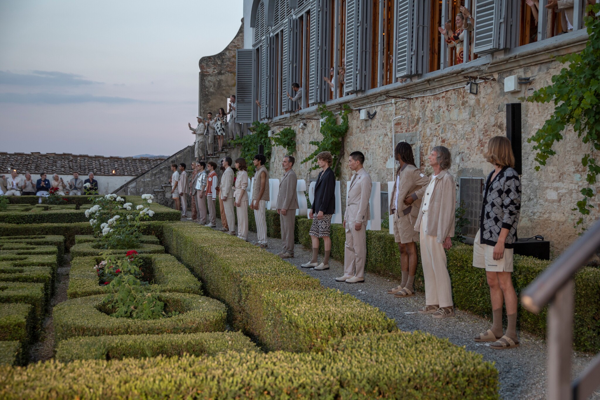 Männliche Models präsentieren Mode und stehen nebeneinander in einem Garten vor einem alten Haus