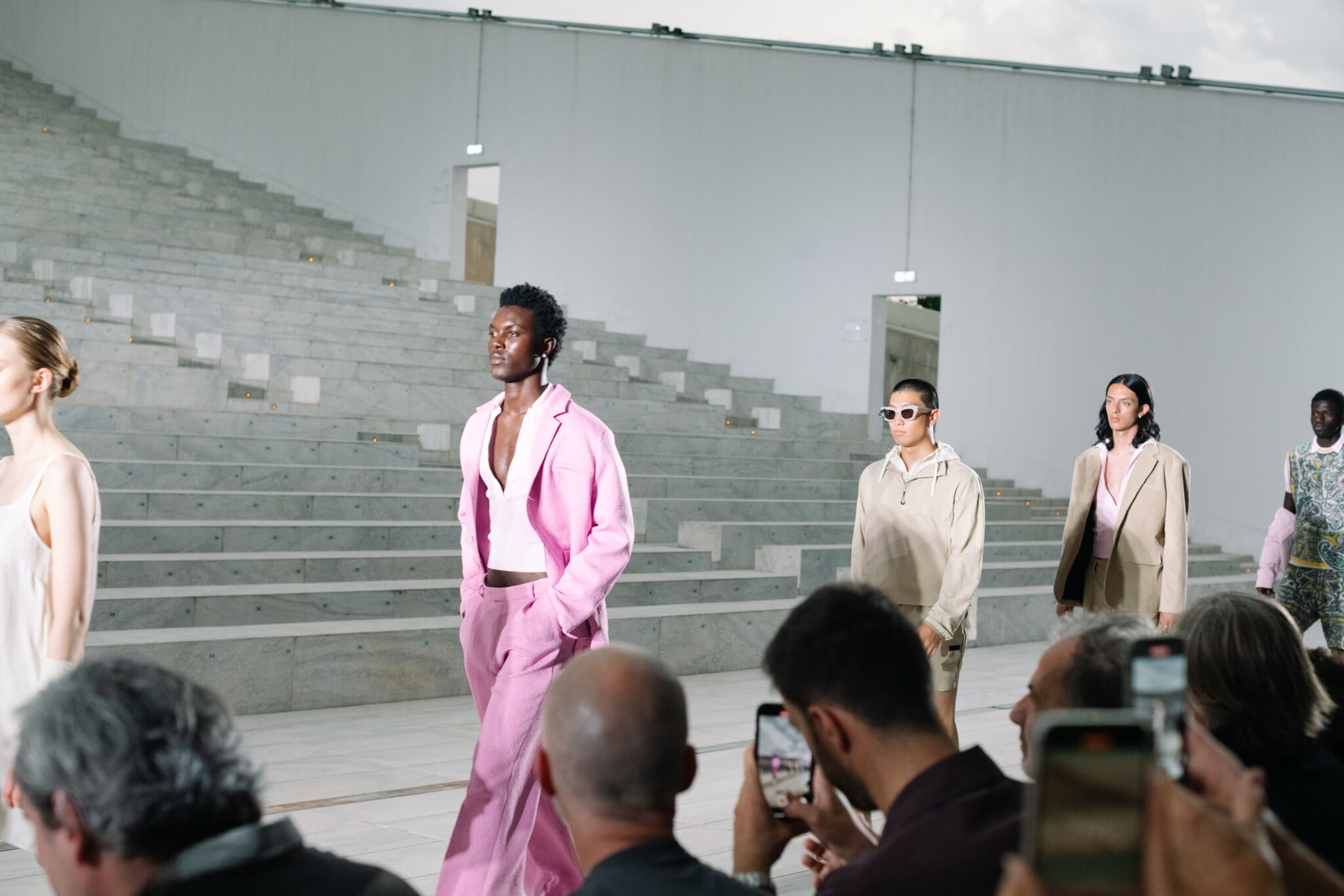 Männliche Models laufen bei einer Fashionshow, im Vordergrund sitzt das Publikum und filmt mit Handys die Show Männliche Models laufen bei einer Fashionshow, im Vordergrund sitzt das Publikum und filmt mit Handys die Show