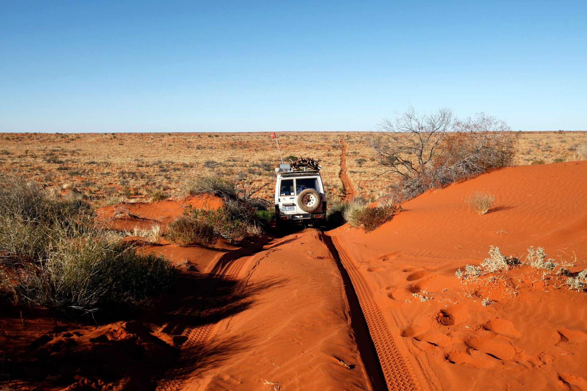 Ein Jeep, der durch eine rote Sanddünenwüste fährt Ein Jeep, der durch eine rote Sanddünenwüste fährt