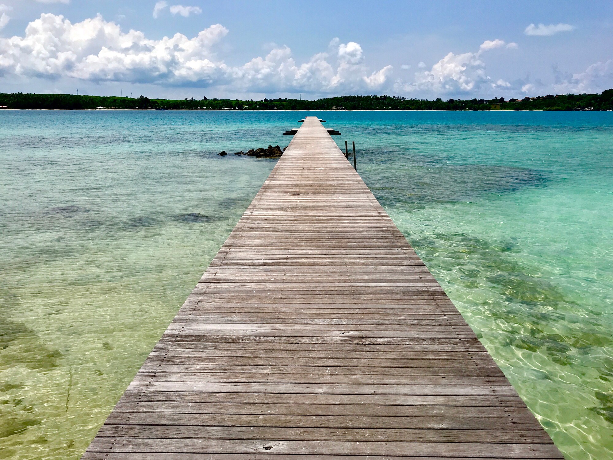 Langer Holzpier, der auf das Meer führt, mit Blick auf eine entfernte Insel Langer Holzpier, der auf das Meer führt, mit Blick auf eine entfernte Insel