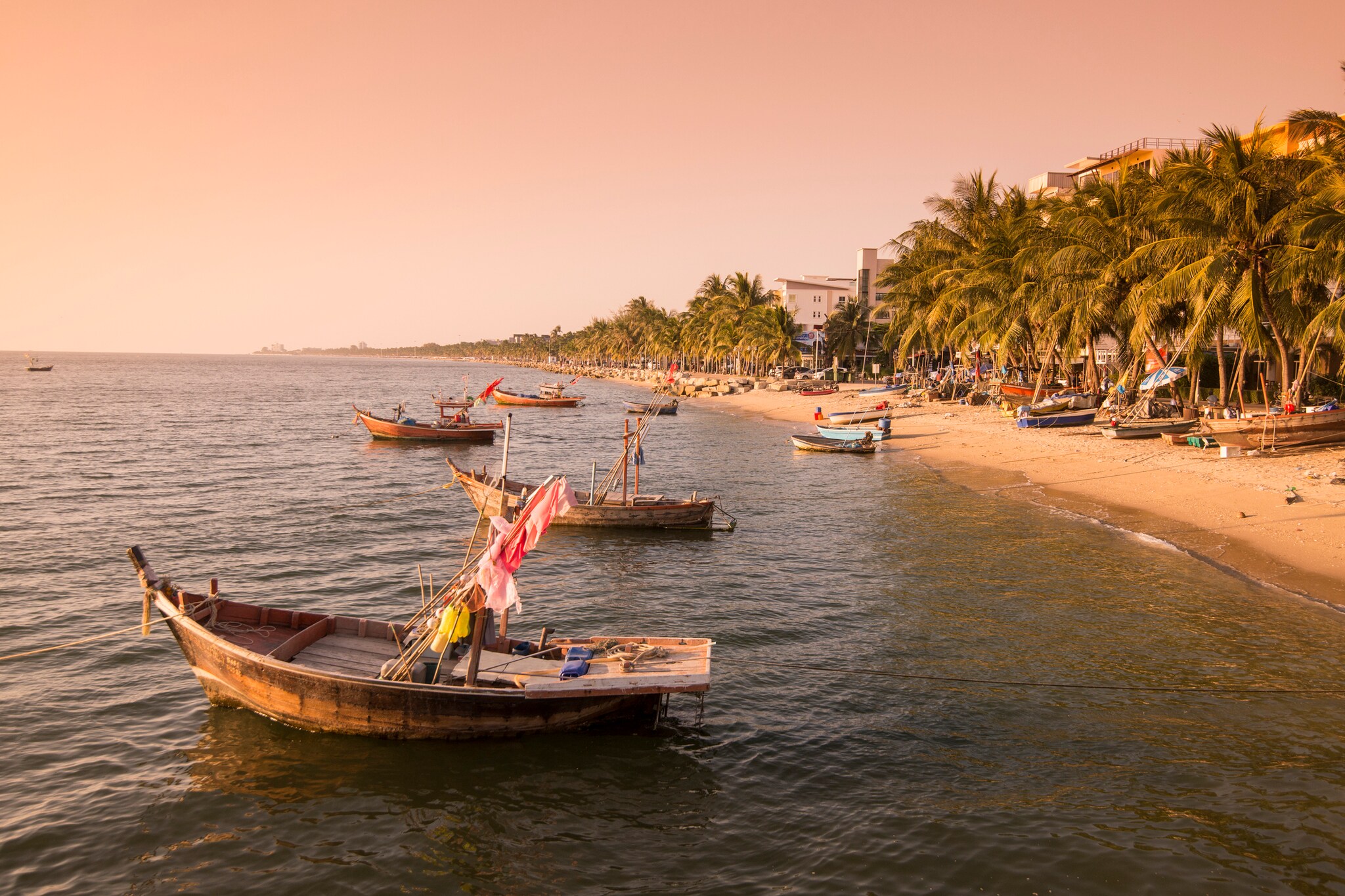 Holzboote auf dem Meer an einem Strand mit Palmen, dahinter Häuser