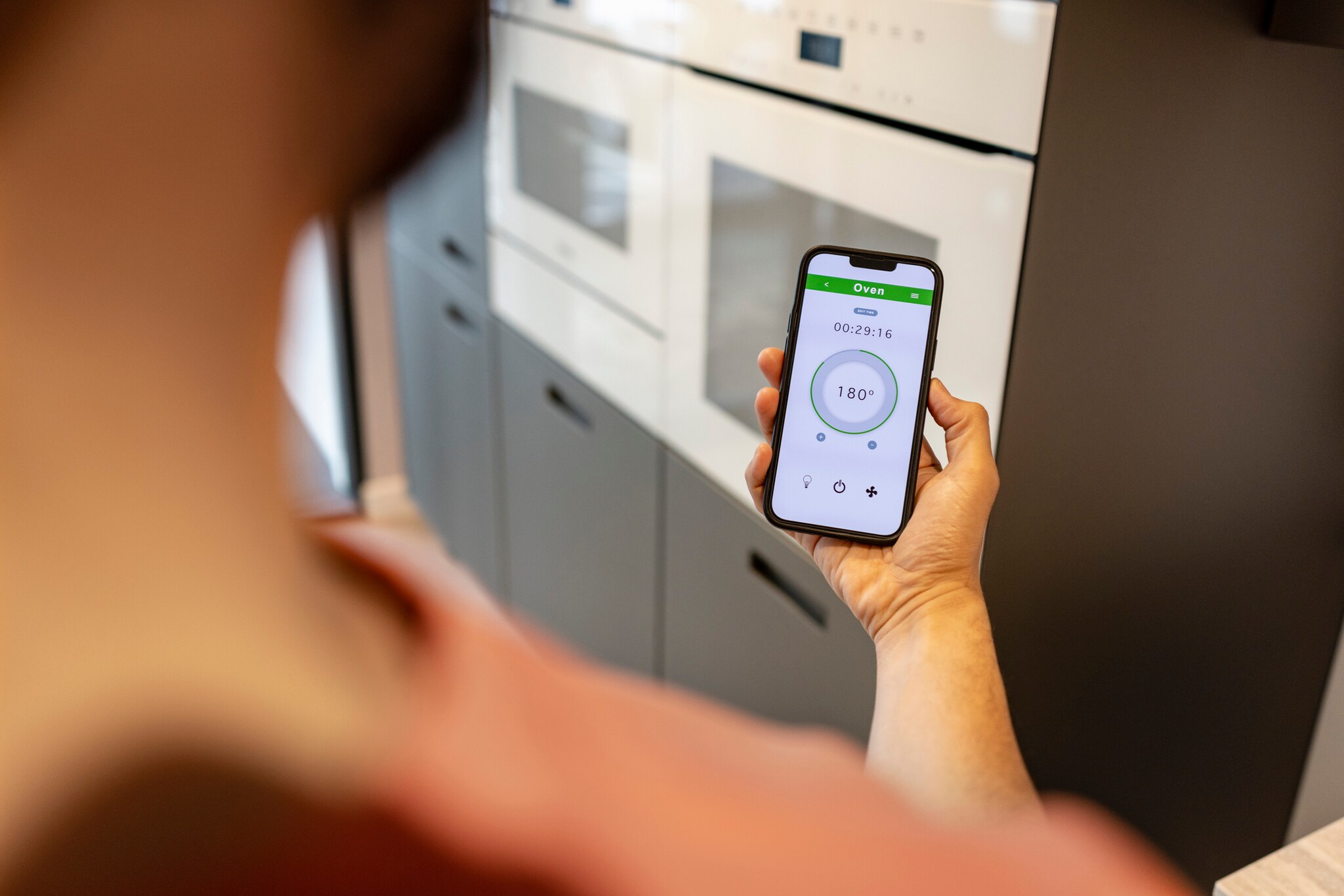 Ein Blick über die Schulter einer Person, die ein Smartphone benutzt, um die Temperatur zu Hause einzustellen.