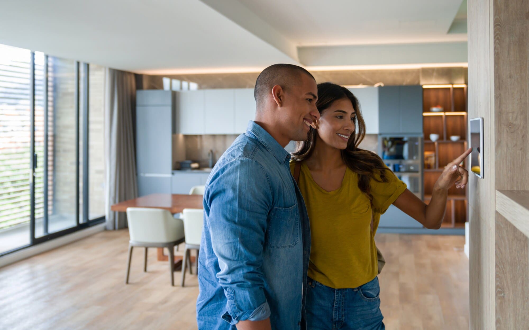 Zwei Personen stehen in einer modern eigenrichteten Wohnung und bedienen einen Touchscreen an der Wand Zwei Personen stehen in einer modern eigenrichteten Wohnung und bedienen einen Touchscreen an der Wand