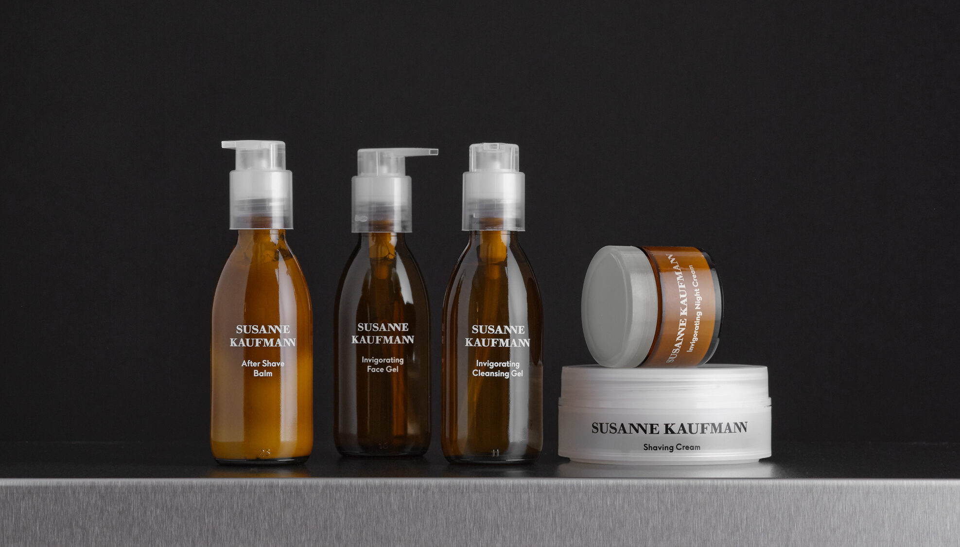 Drei Kosmetikflaschen und zwei Tiegel vor schwarzem Hintergrund, die Rasurprodukte von Susanne Kaufmann enthalten Drei Kosmetikflaschen und zwei Tiegel vor schwarzem Hintergrund, die Rasurprodukte von Susanne Kaufmann enthalten