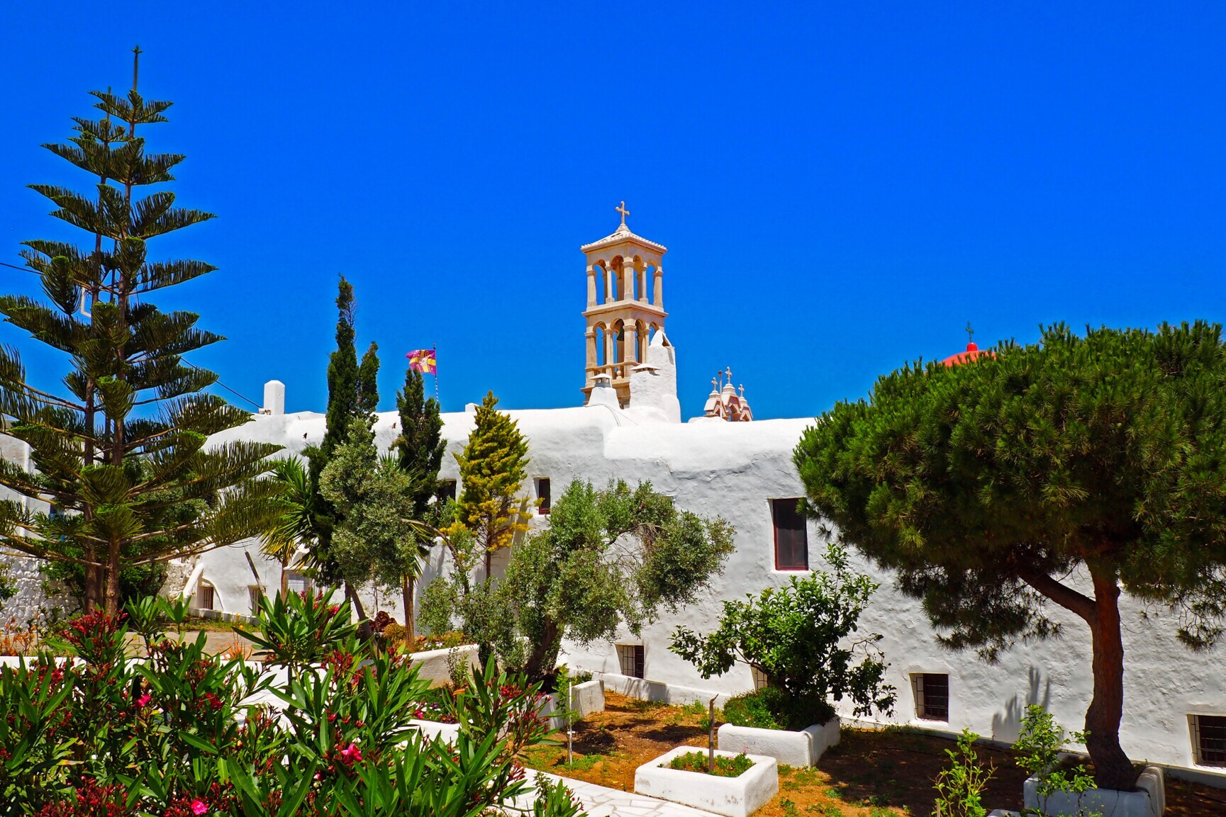 Das Kloster Panagia Tourliani auf Mykonos, davor ein Garten mit Büschen und Bäumen