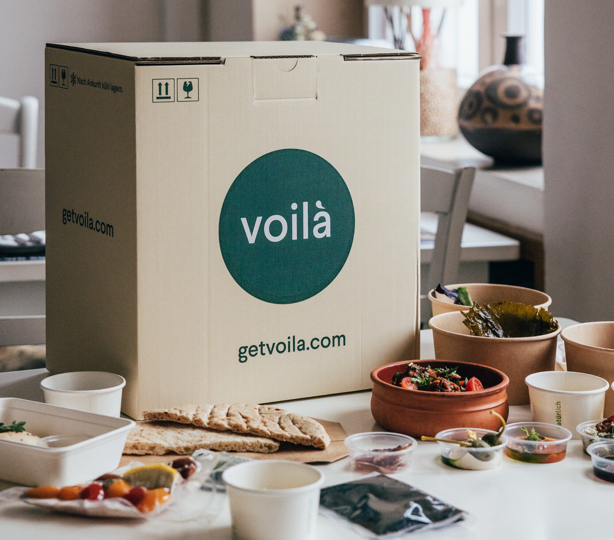 Kochbox von Voilà auf einem Tisch, eingerahmt von Schalen mit Zutaten