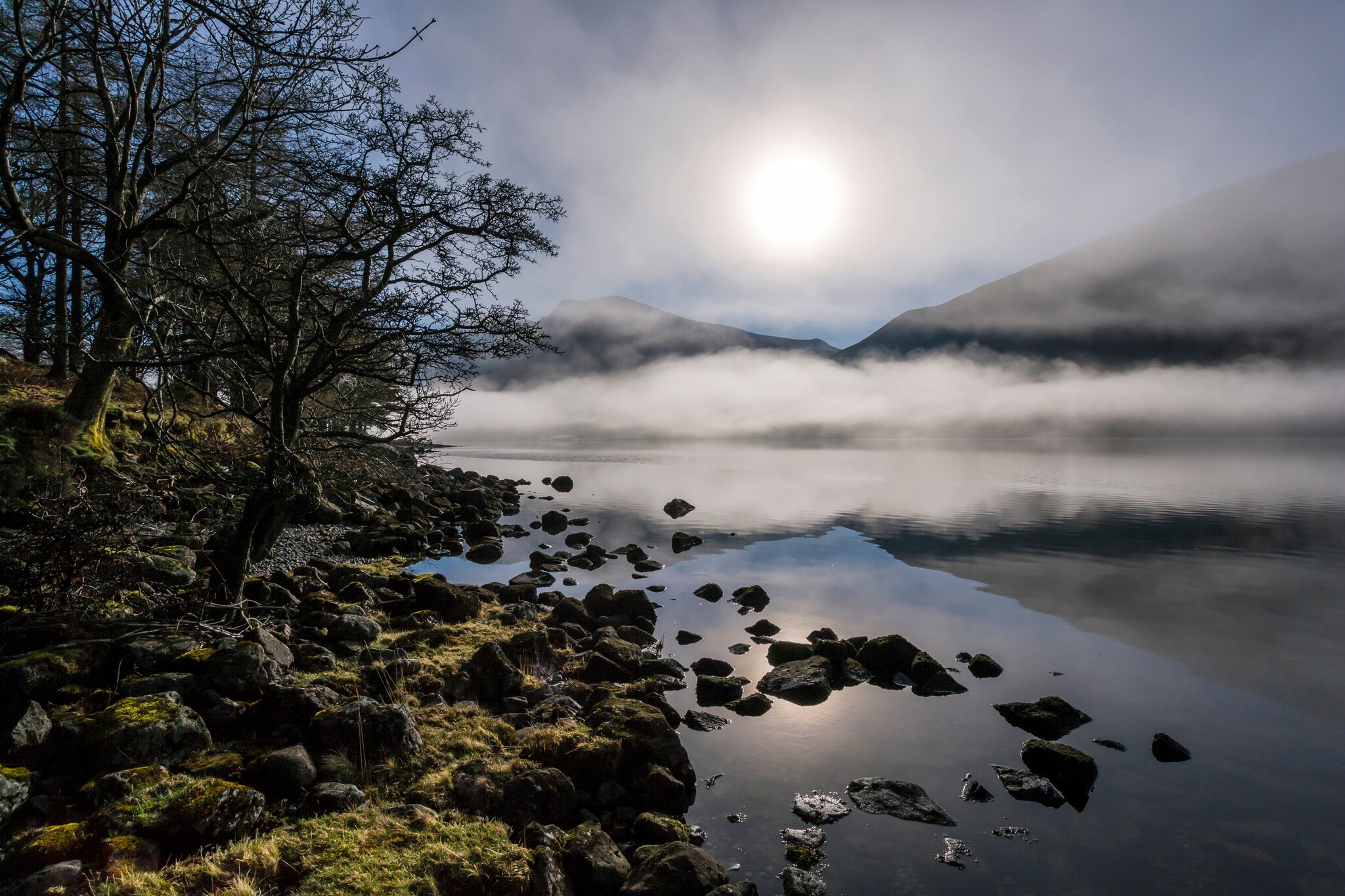 Nebelschwaden über einem See, im Hintergrund Berge