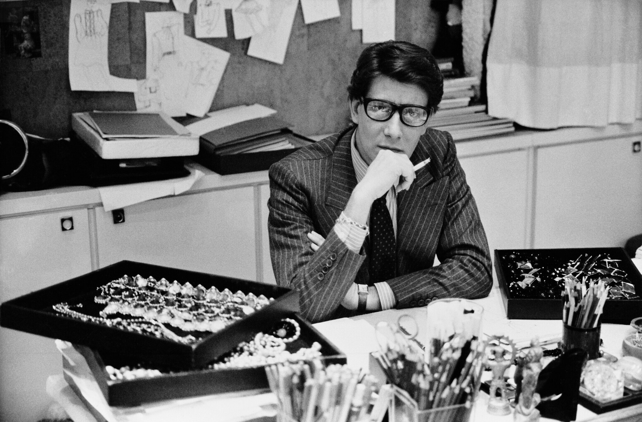 Schwarz-weiß-Aufnahme von Yves Saint Laurent an einem Schreibtisch in Paris 1986.