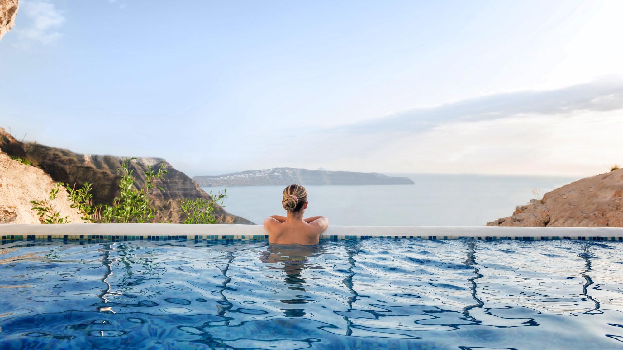 Rückansicht einer Frau in einem Infinitypool mit Blick aufs Meer Rückansicht einer Frau in einem Infinitypool mit Blick aufs Meer