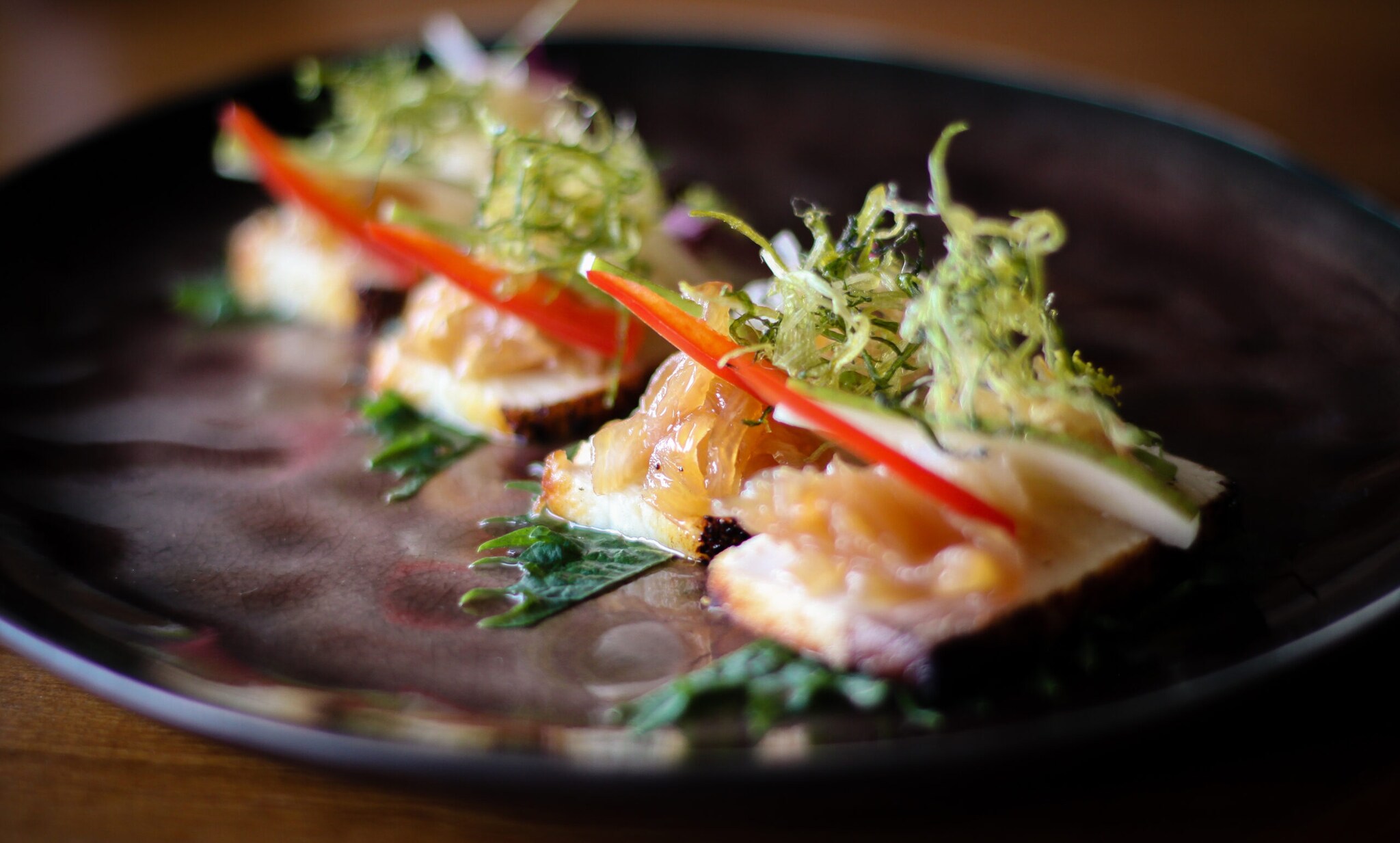 Ein japanisches Hamachi Gericht mit Salatgarnitur auf einem schwarzen Teller angerichtet