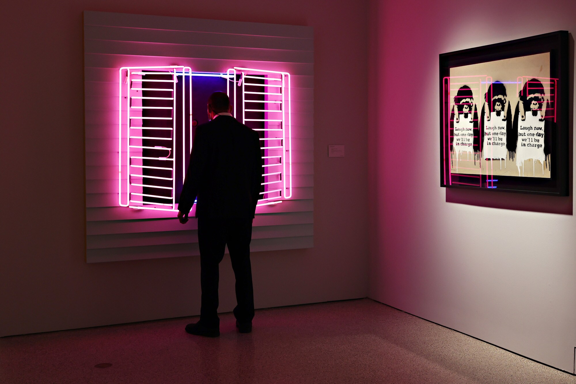 Eine Person schaut sich ein Kunstwerk in der Form eines Fensters aus Neonröhren an der Wand eines Ausstellungsraums an