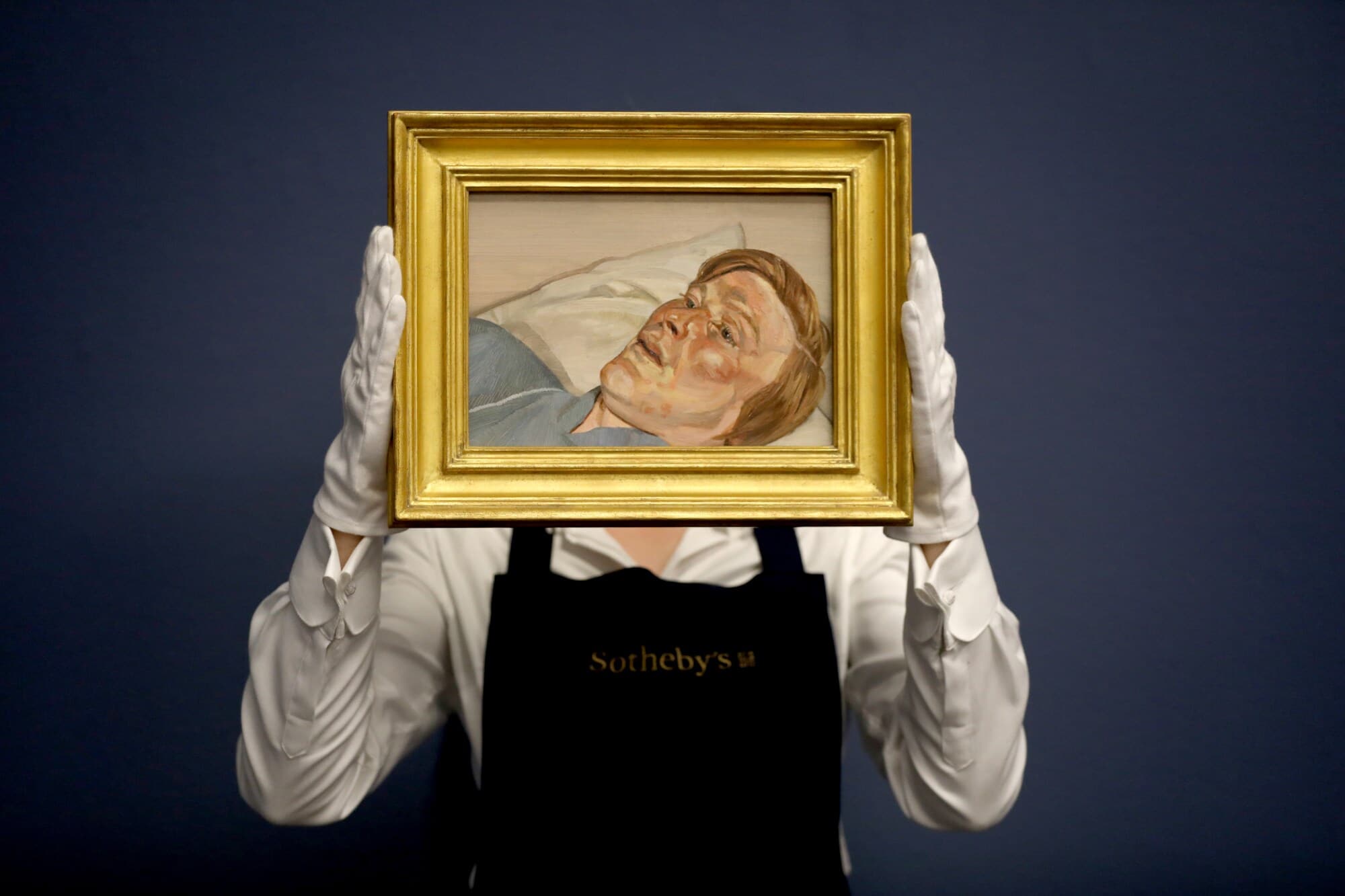 Eine Mitarbeiterin von Sotheby’s hält mit weißen Handschuhen ein kleines Gemälde von Lucian Freud in einem goldenen Rahmen hoch