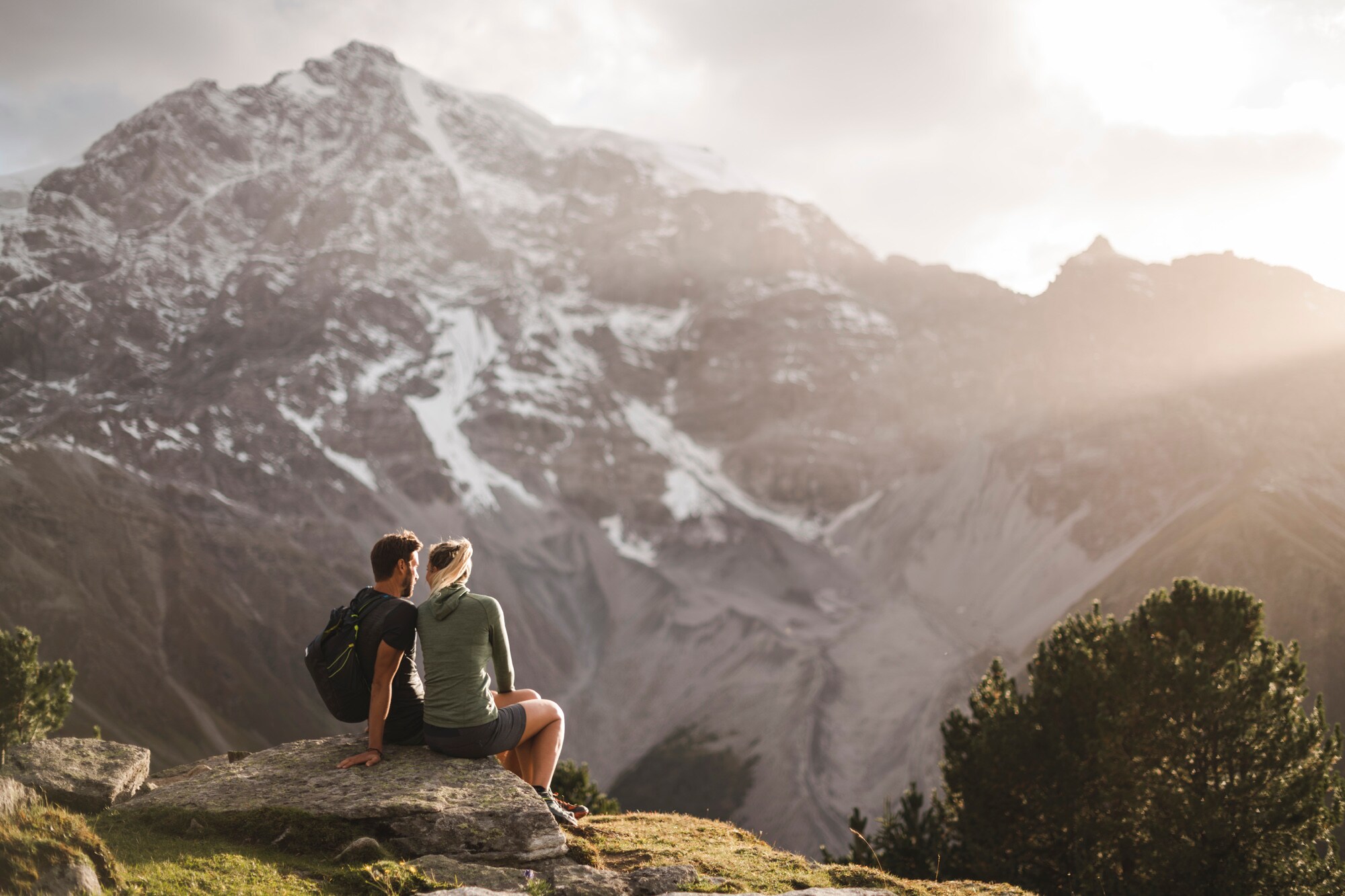Zwei Personen sitzen im Nationalpark Stilfserjoch auf einem Stein und blicken auf ein Bergmassiv.