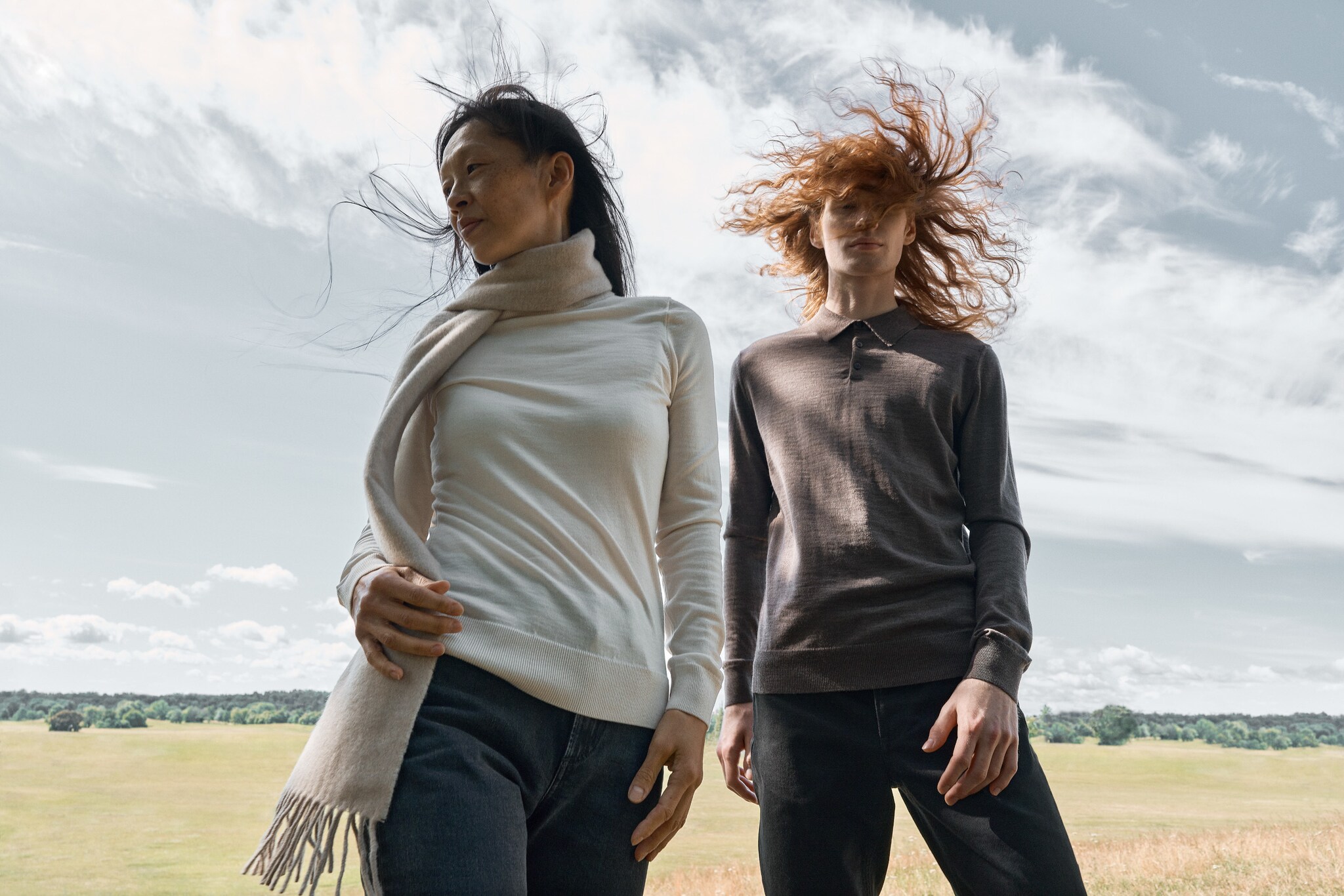 Zwei Frauen mit wehenden Haaren, die in Hose und Pullover gekleidet sind, eine mit Schal Zwei Frauen mit wehenden Haaren, die in Hose und Pullover gekleidet sind, eine mit Schal