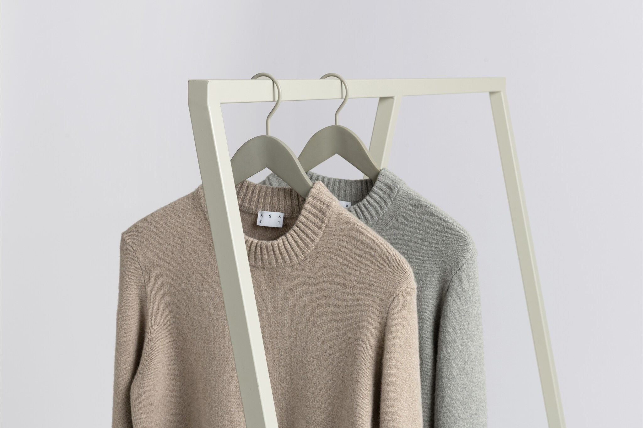 Zwei Pullover in Grau und Beige, die an einer Kleiderstange hängen