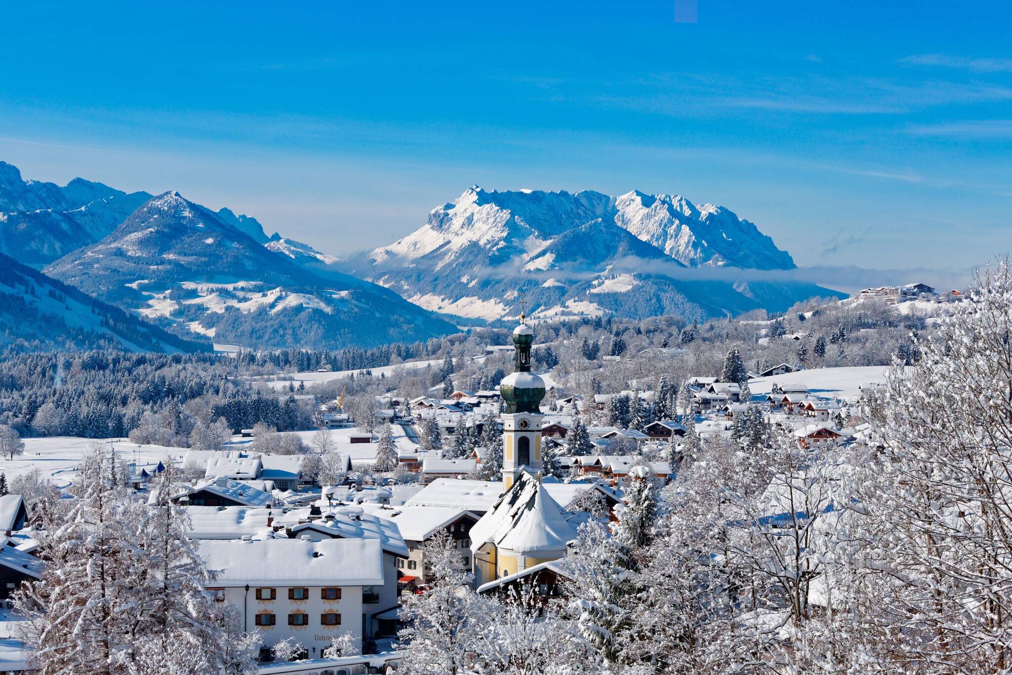 Verschneite Ortschaft mit Kirchturm vor Bergpanorama Verschneite Ortschaft mit Kirchturm vor Bergpanorama