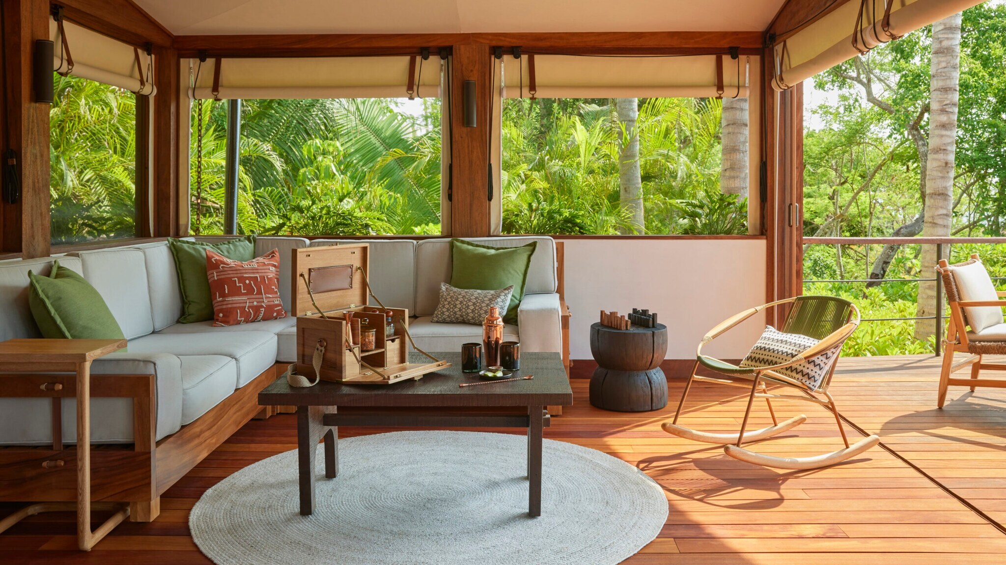 Wohnraum eines Glamping-Zelts mit Sofa und Tisch und offenen Fenstern, durch die grüner Wald zu sehen ist
