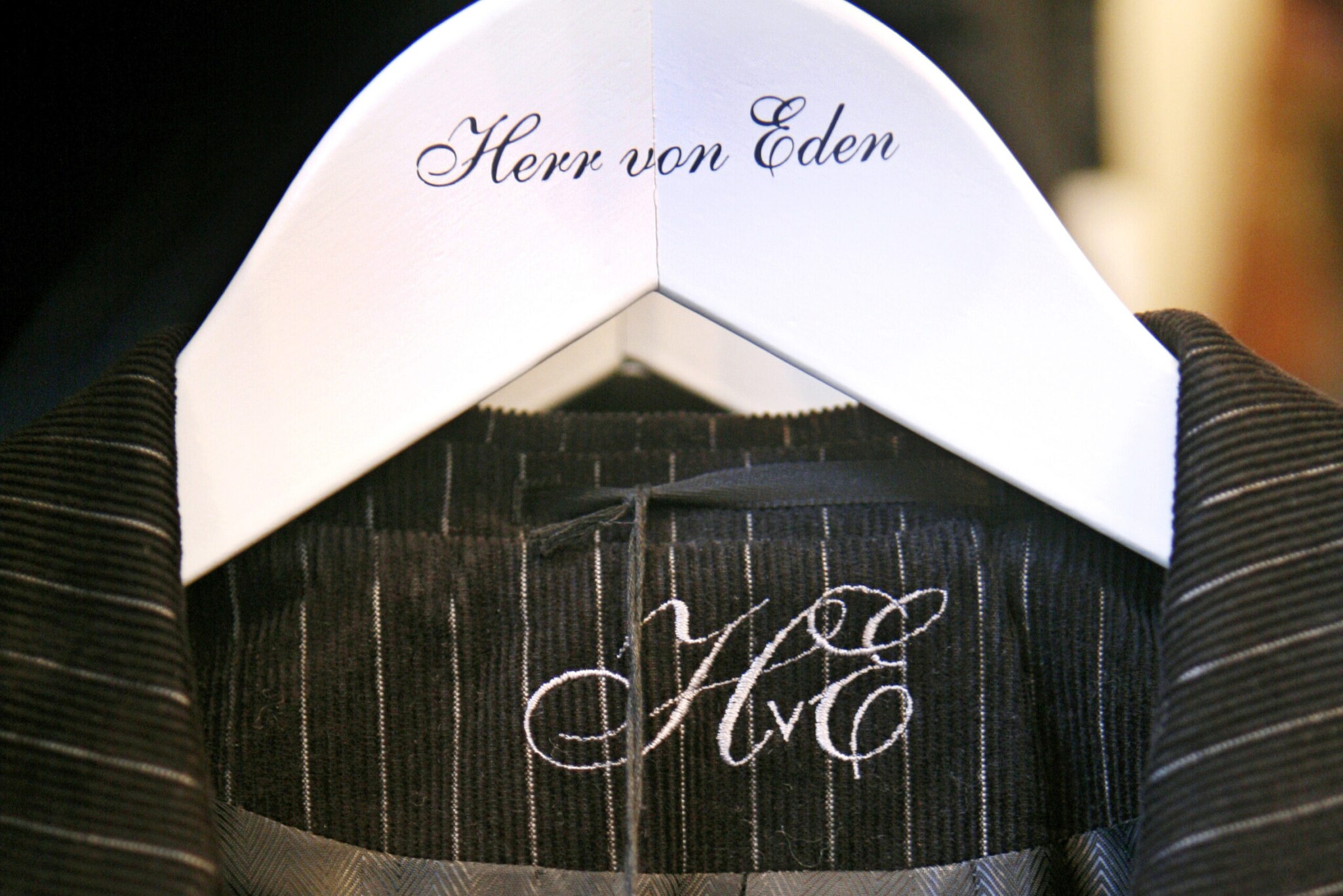 Detailaufnahme eines Nadelstreifenanzugs auf einem weißen Kleiderbügel mit einer geschnörkelten Aufschrift