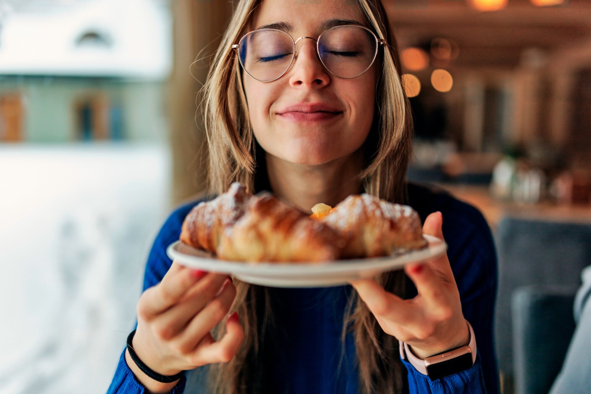 Junge Frau mit leichtem Lächeln und geschlossenen Augen, die vor ihr Gesicht einen Teller mit Gebäck hält Junge Frau mit leichtem Lächeln und geschlossenen Augen, die vor ihr Gesicht einen Teller mit Gebäck hält