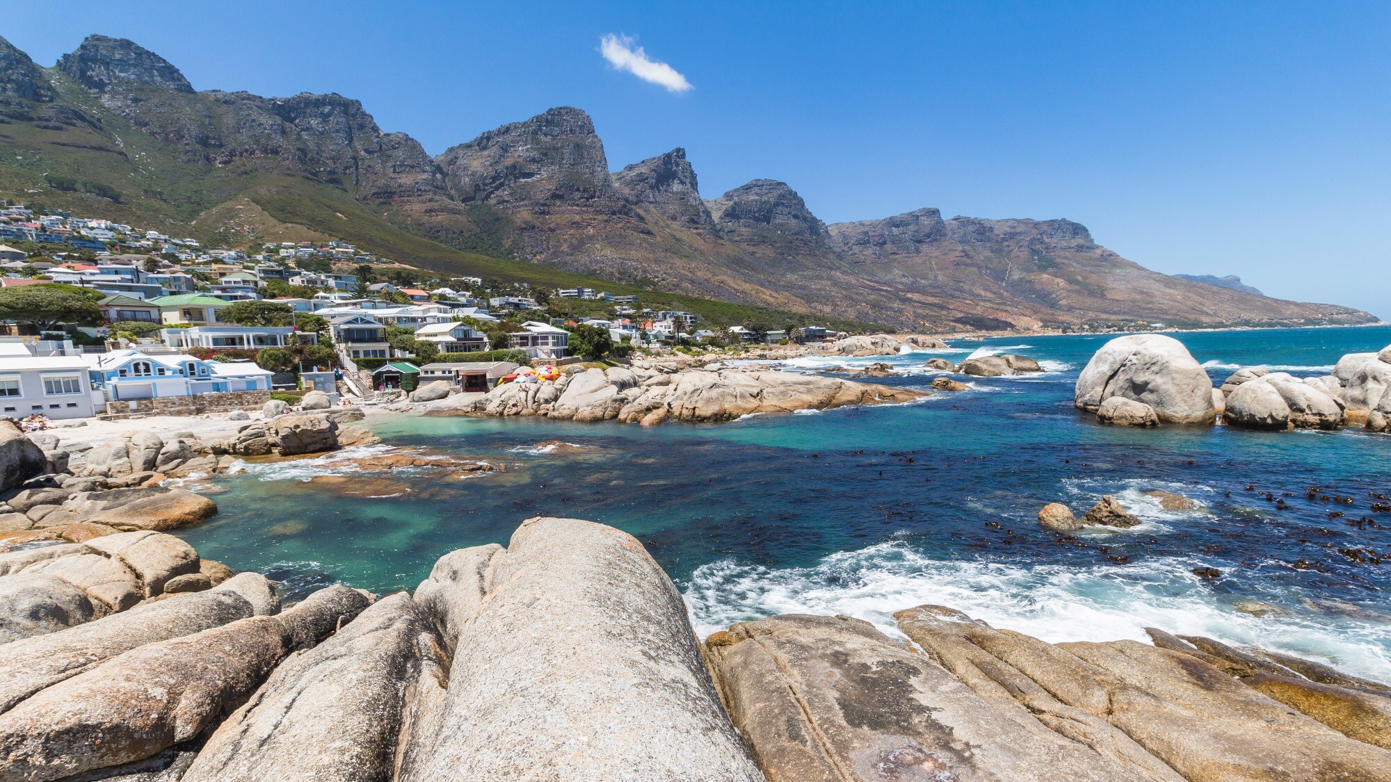 Felsiger Strand bei Kapstadt an einer Ortschaft mit Blick auf die Gebirgskette Zwölf Apostel