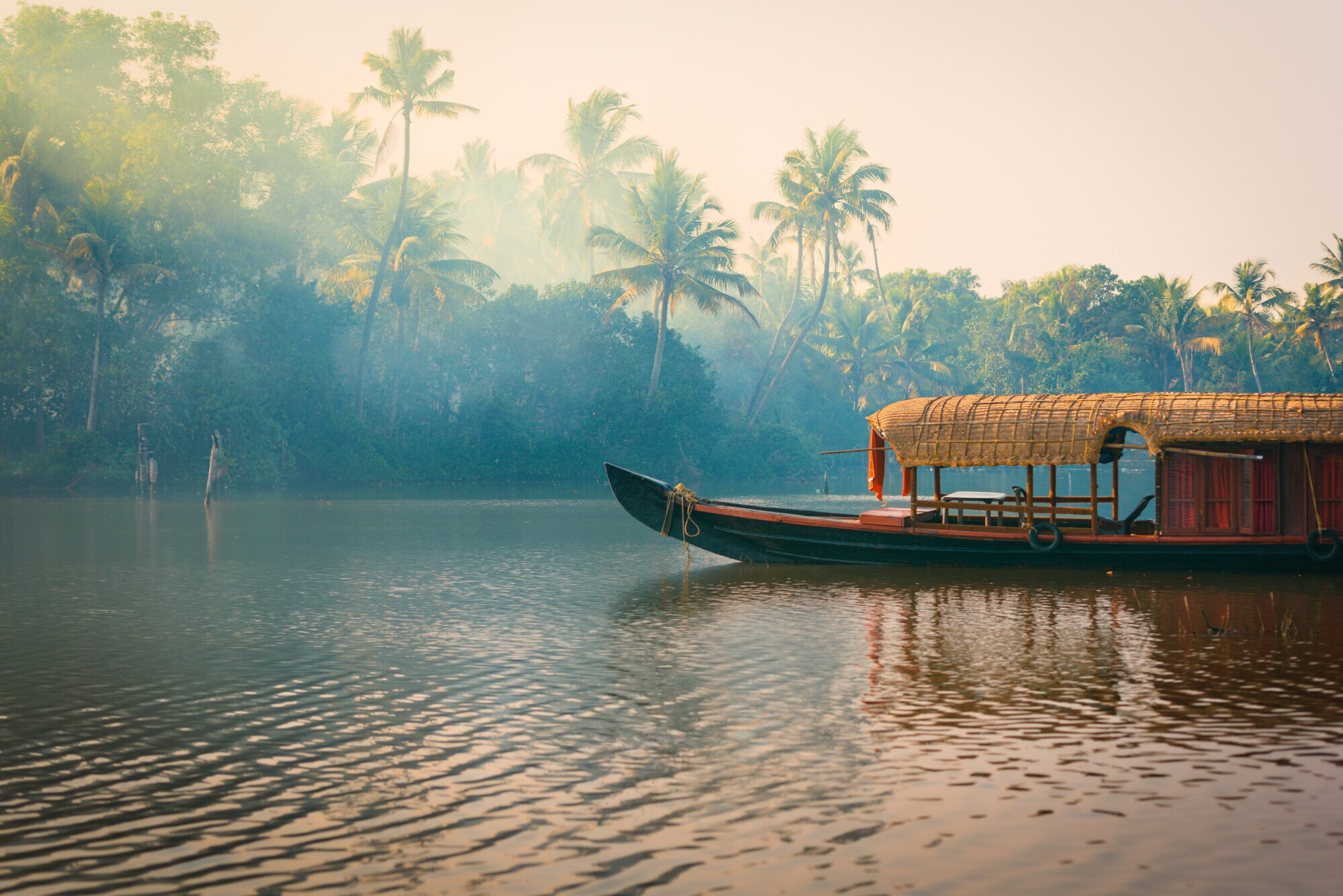 Ein traditionelles Hausboot bei Sonnenuntergang in den Backwaters im Palmenduschungel von Kerala