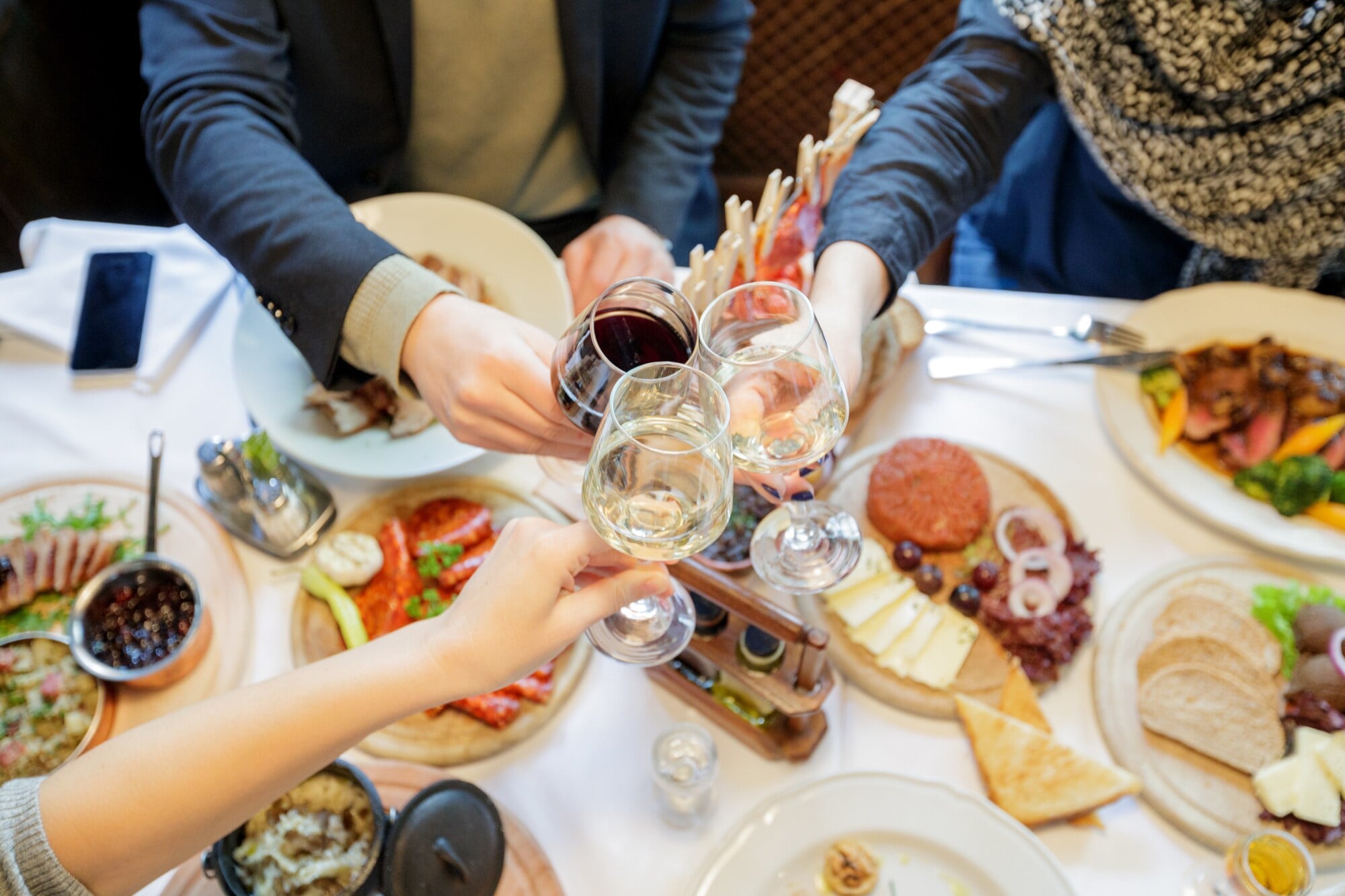 Drei Personen stoßen über einem reich gedeckten Tisch mit ihren Gläsern zusammen an Drei Personen stoßen über einem reich gedeckten Tisch mit ihren Gläsern zusammen an