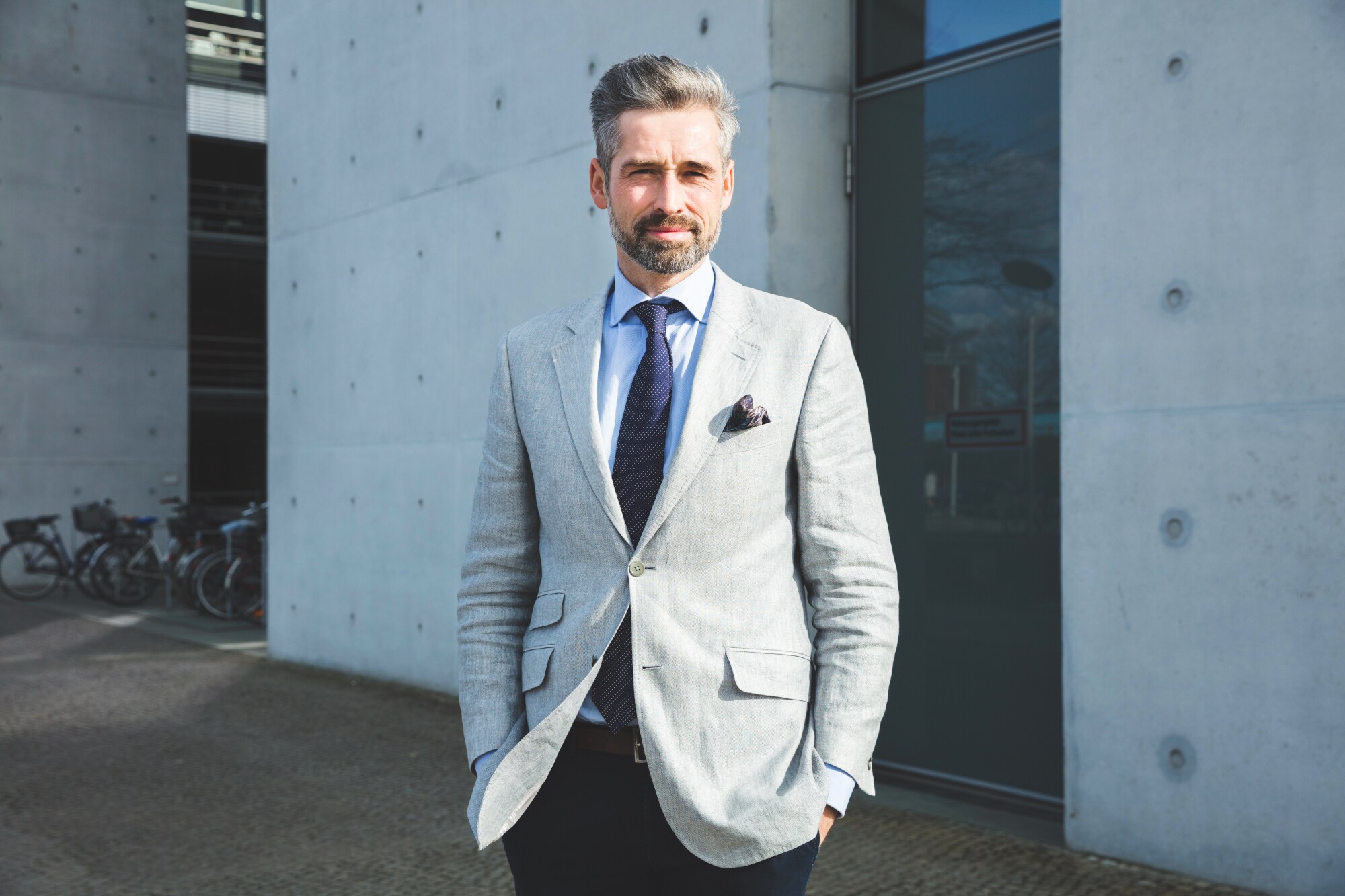 Ein Mann im hellen Sakko und dunkler Krawatte steht vor einem modernen Gebäude