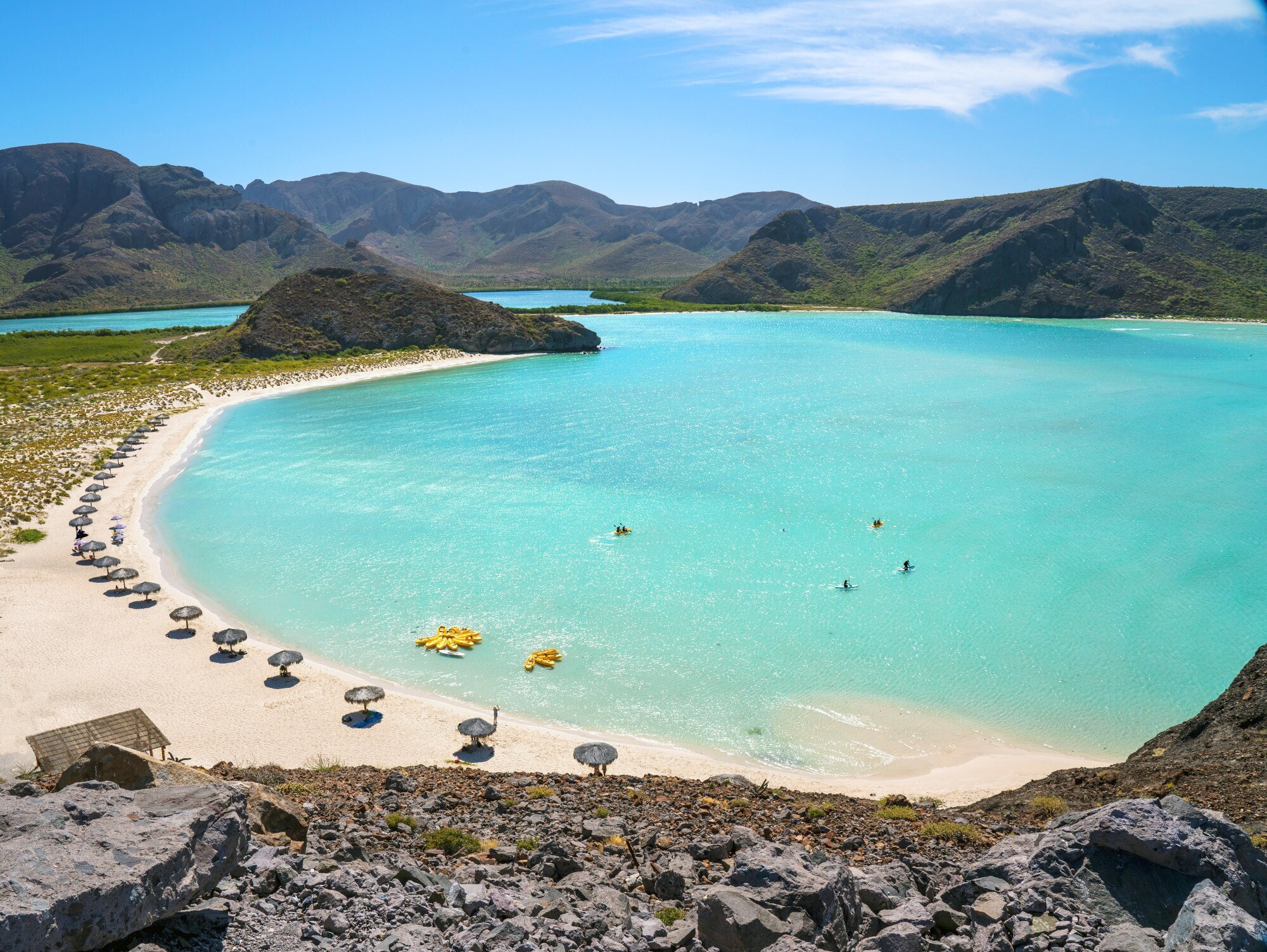 Eine von Hügeln umgebene Badebucht mit Sonnenschirmen