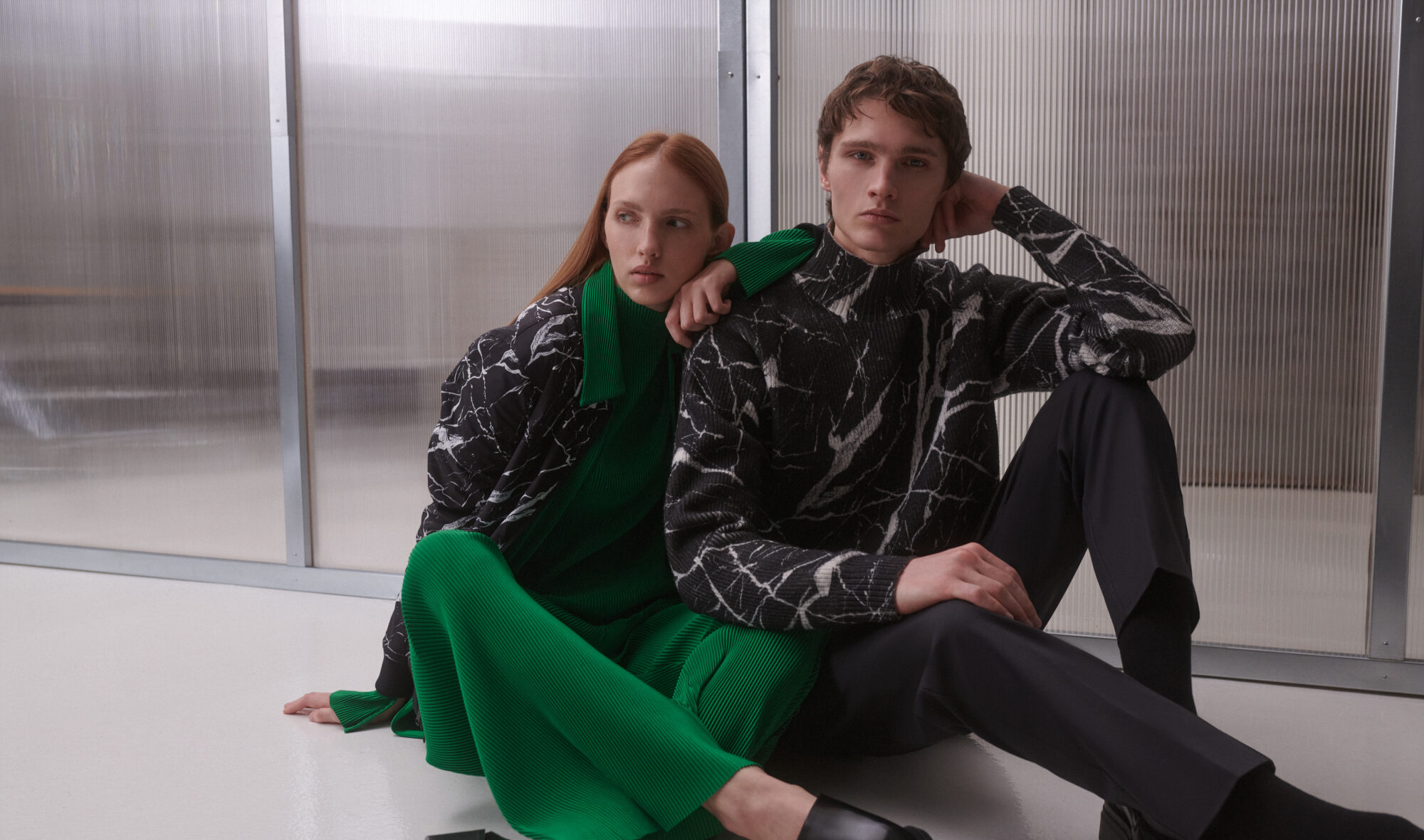 Zwei Personen mit schwarz-grüner Kleidung, die auf dem Boden sitzen und sich aneinander anlehnen Zwei Personen mit schwarz-grüner Kleidung, die auf dem Boden sitzen und sich aneinander anlehnen