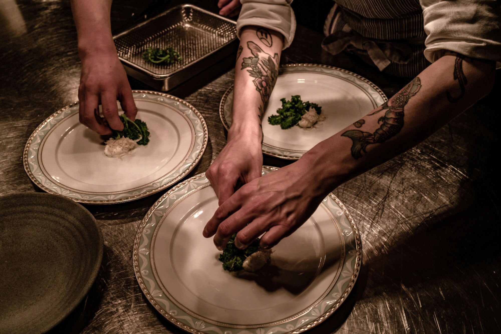 Nahaufnahme von Händen beim Anrichten von Speisen auf großen, weißen Tellern in einer Restaurantküche.