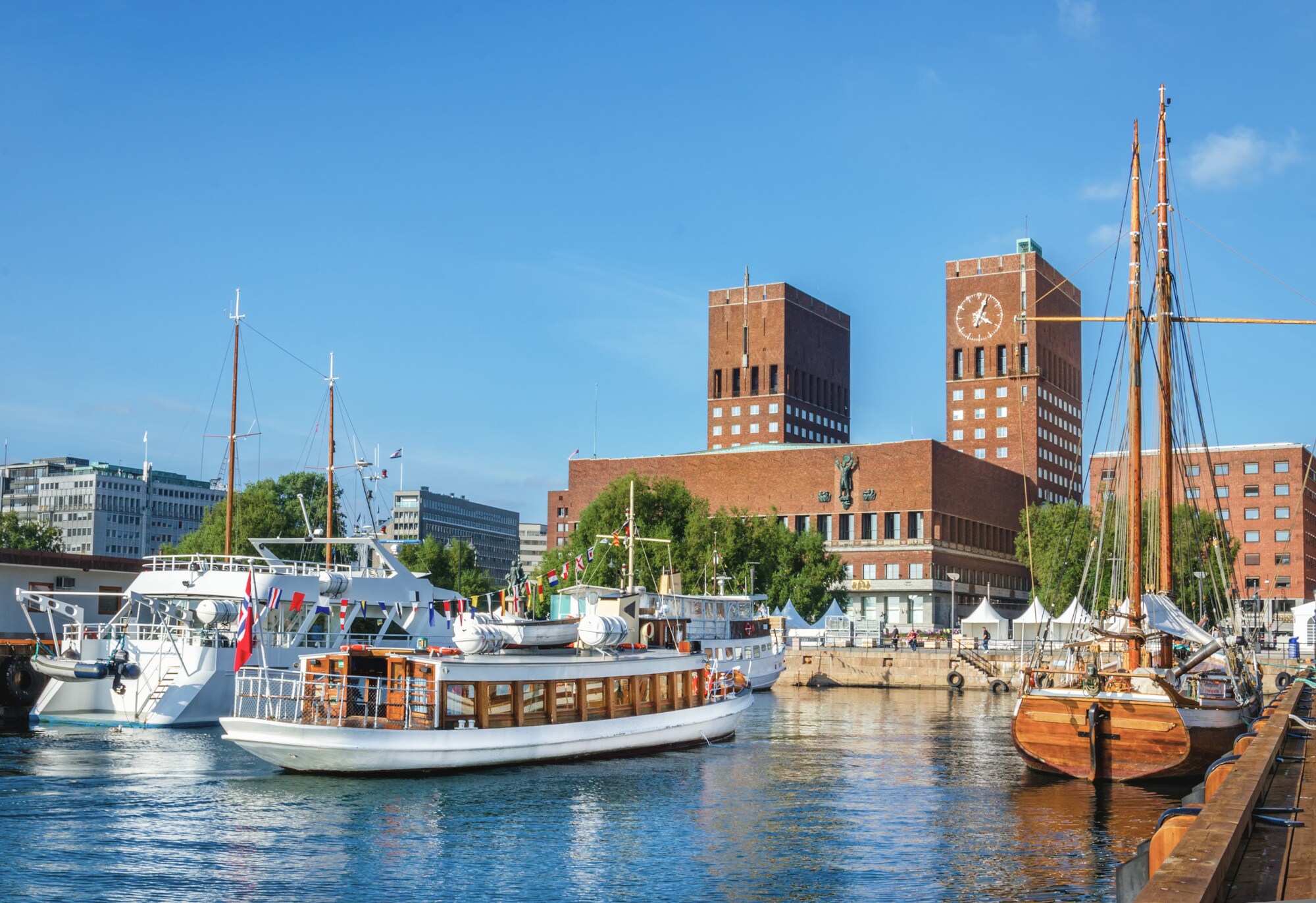Blick auf das rote Rathaus von Oslo mit Backsteintürmen vom Wasser aus, im Vordergrund Segelboote