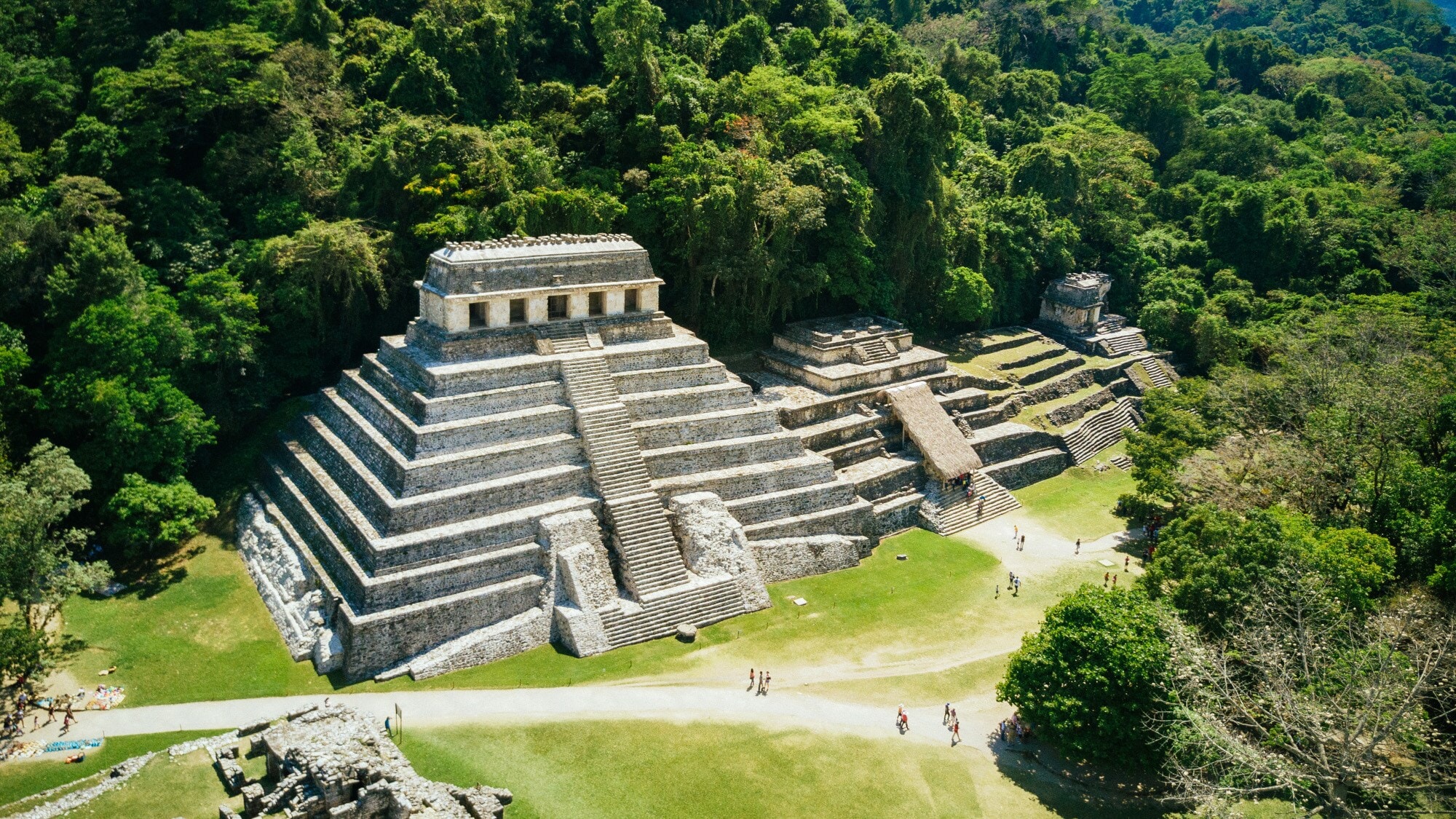 Luftaufnahme einer Treppenpyramide auf einer archäologischen Ruinenstätte mit Besuchern im Urwald Luftaufnahme einer Treppenpyramide auf einer archäologischen Ruinenstätte mit Besuchern im Urwald