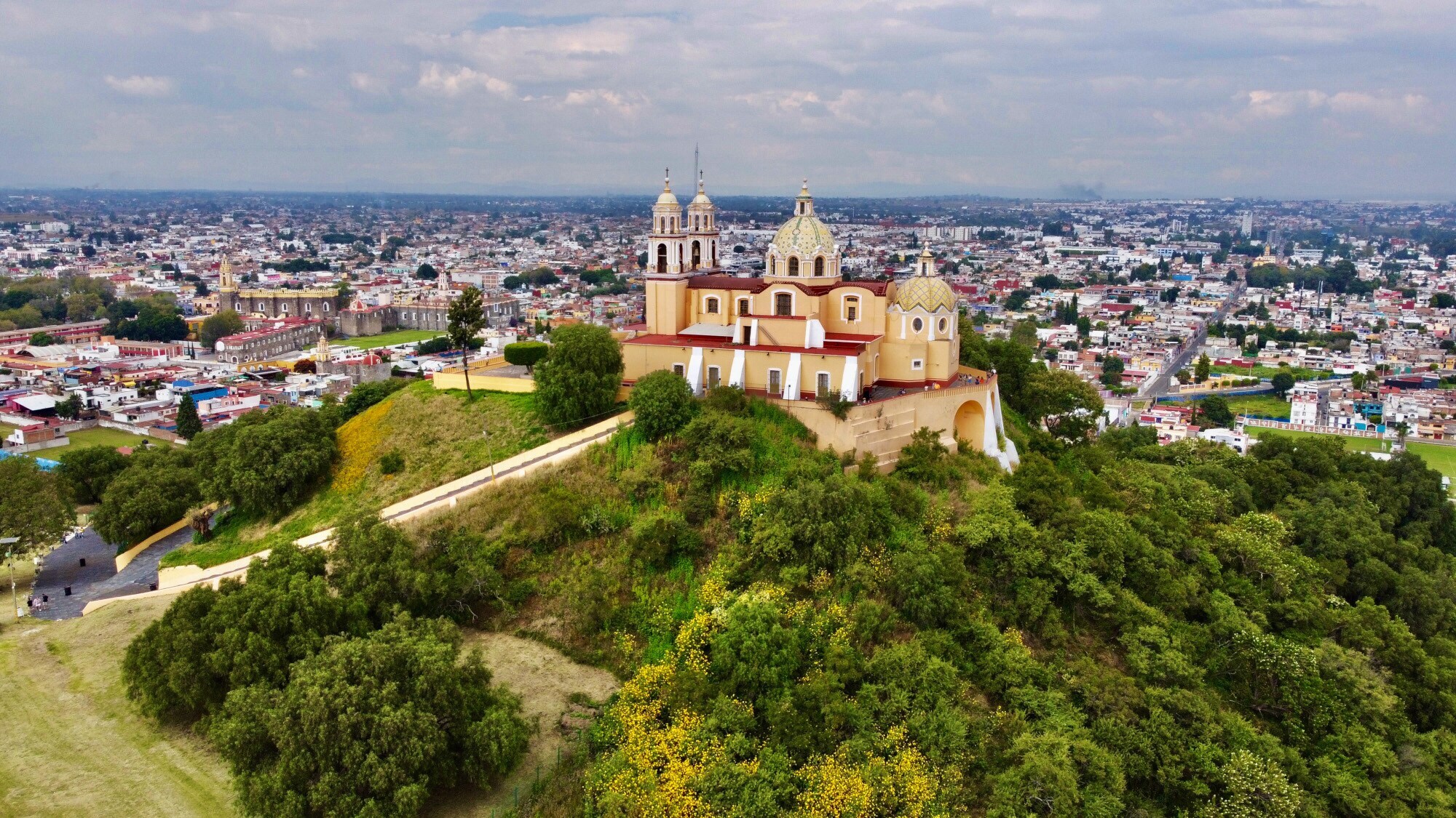 Eine Kirche auf einer mit Bäumen bewachsenen Pyramide vor Stadtpanorama