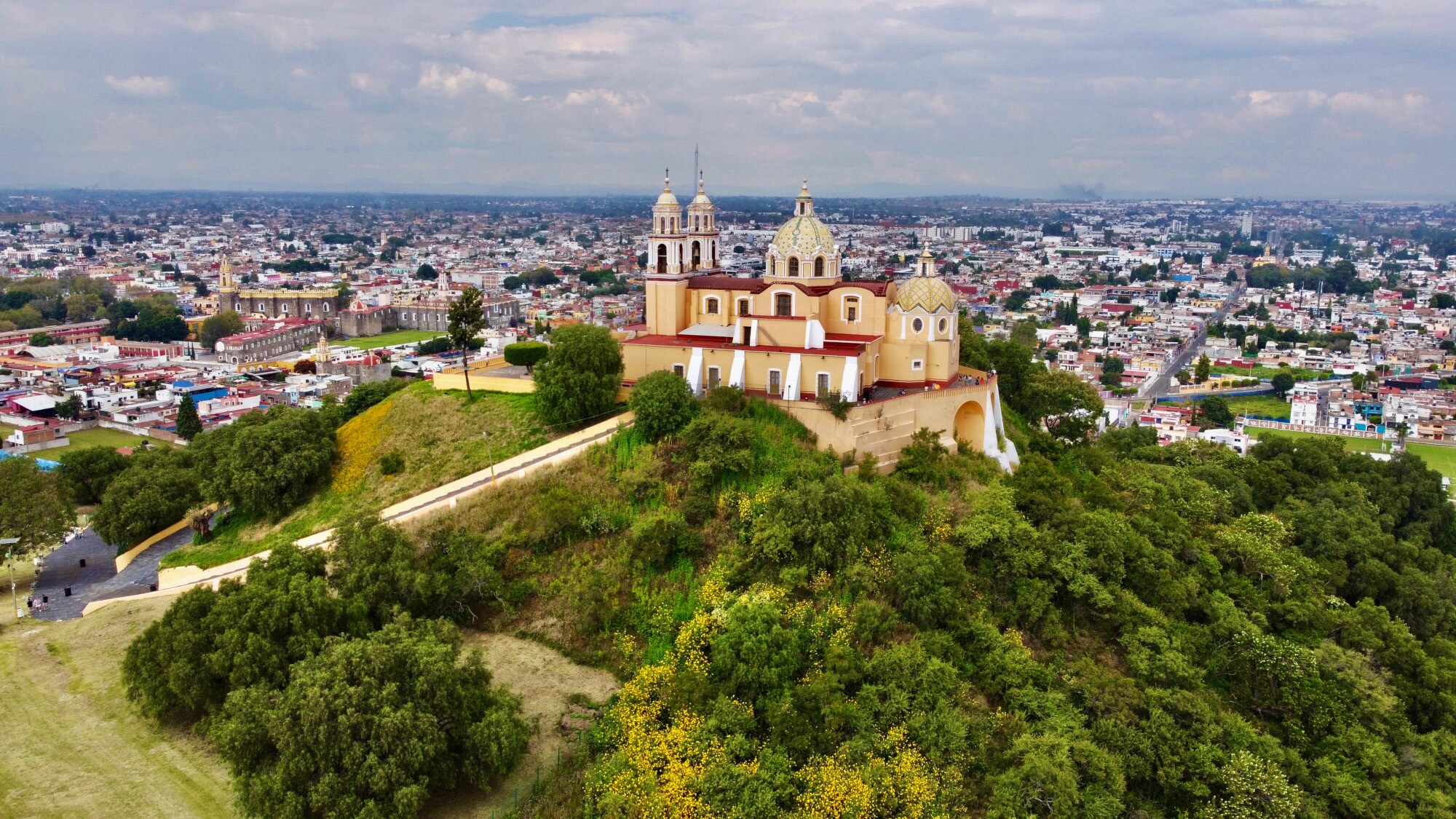 Eine Kirche auf einer mit Bäumen bewachsenen Pyramide vor Stadtpanorama Eine Kirche auf einer mit Bäumen bewachsenen Pyramide vor Stadtpanorama