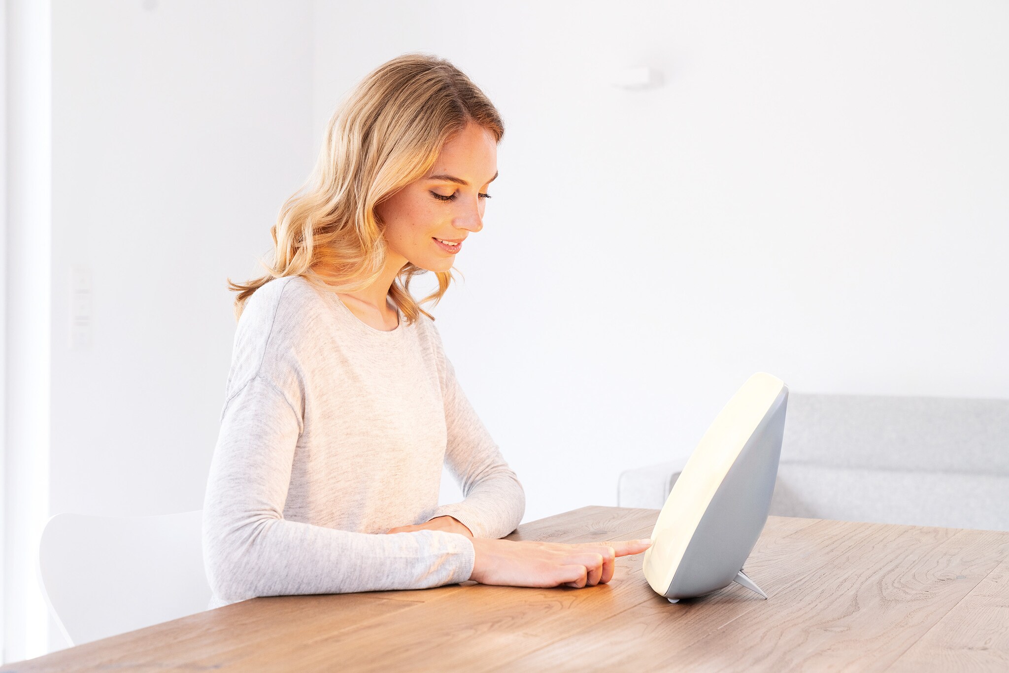 Eine junge Frau sitzt an einem Tisch vor einer Tageslichtlampe