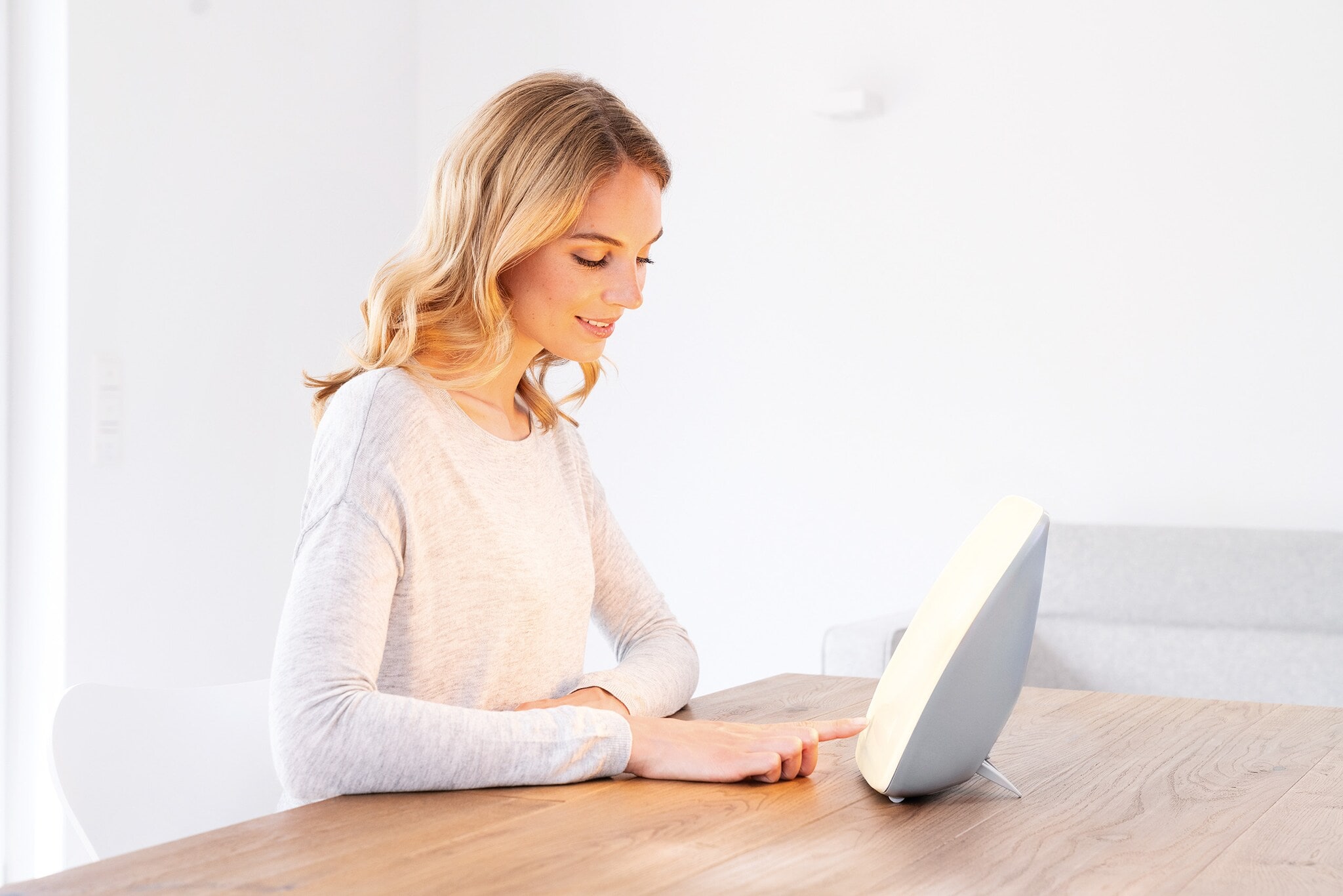 Eine junge Frau sitzt an einem Tisch vor einer Tageslichtlampe Eine junge Frau sitzt an einem Tisch vor einer Tageslichtlampe