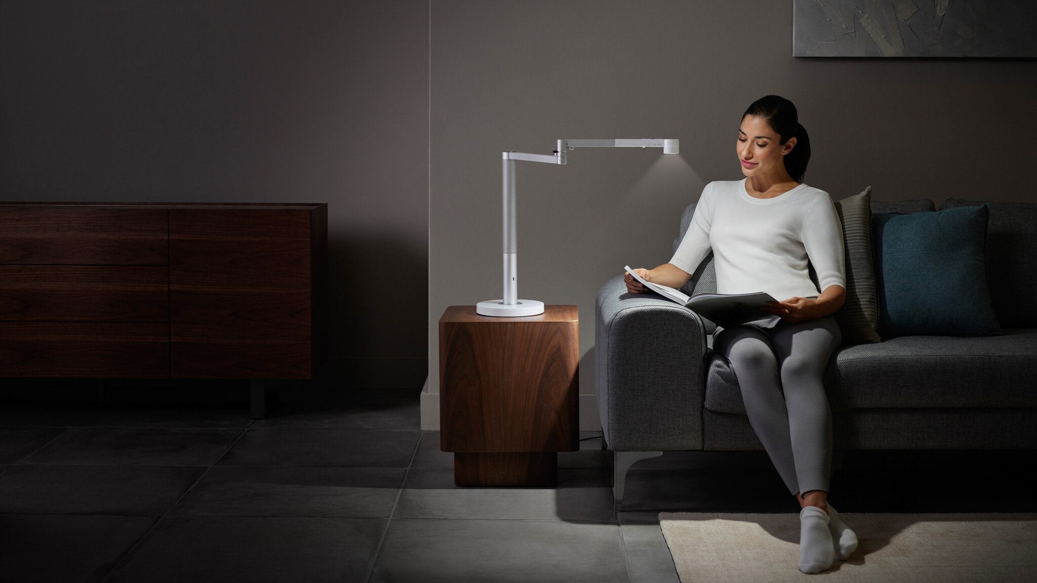 Eine Frau liest auf einem Sofa im Licht einer verstellbaren Tageslichtlampe Eine Frau liest auf einem Sofa im Licht einer verstellbaren Tageslichtlampe