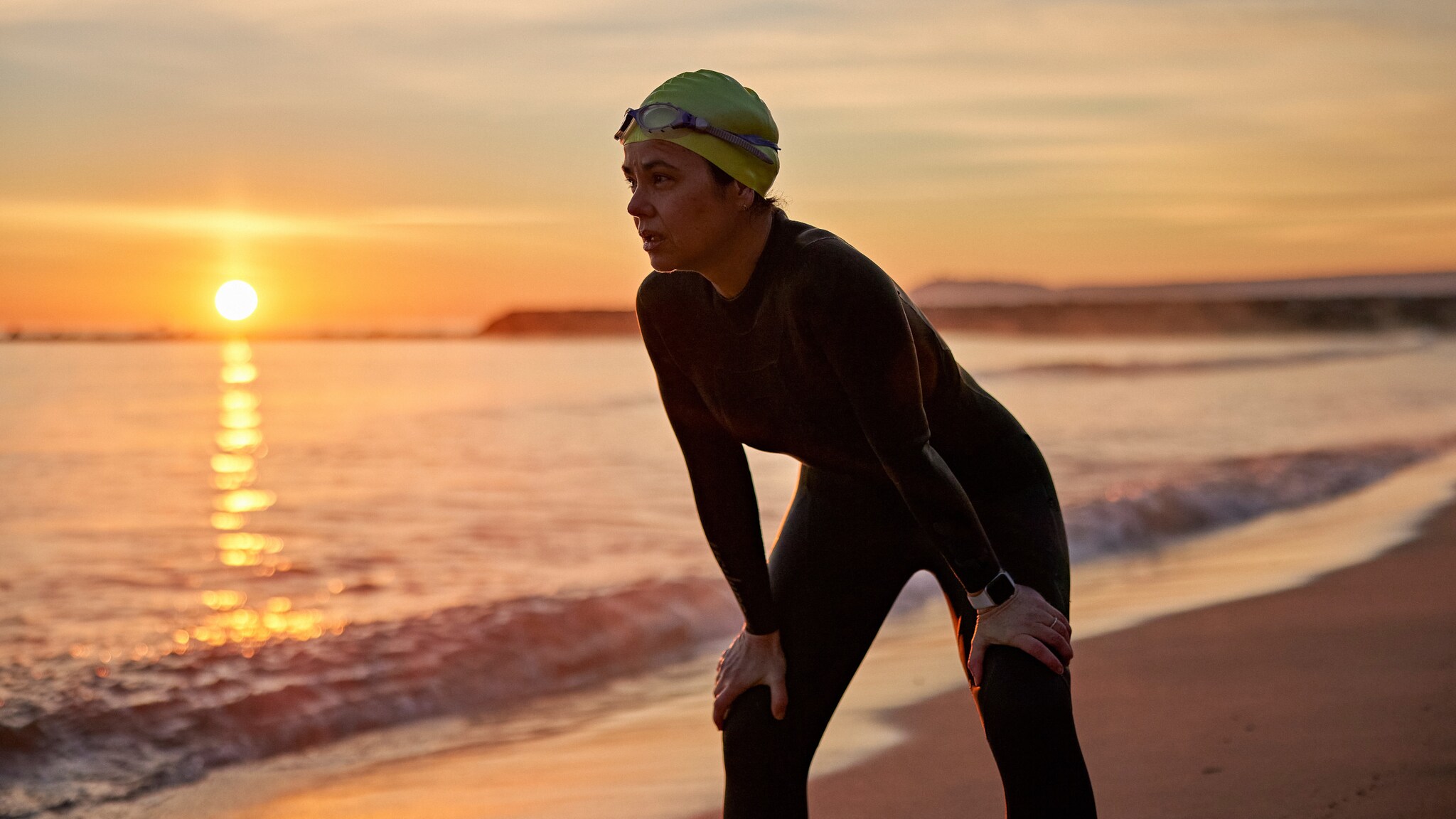 Eine Triathletin ruht nach dem Schwimmen in der Morgendämmerung am Strand aus